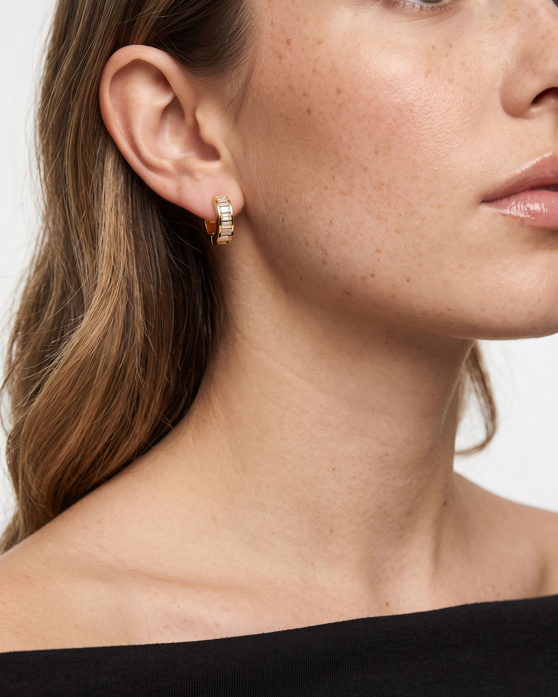 Close-up of a woman wearing gold hoop earrings with a plain background