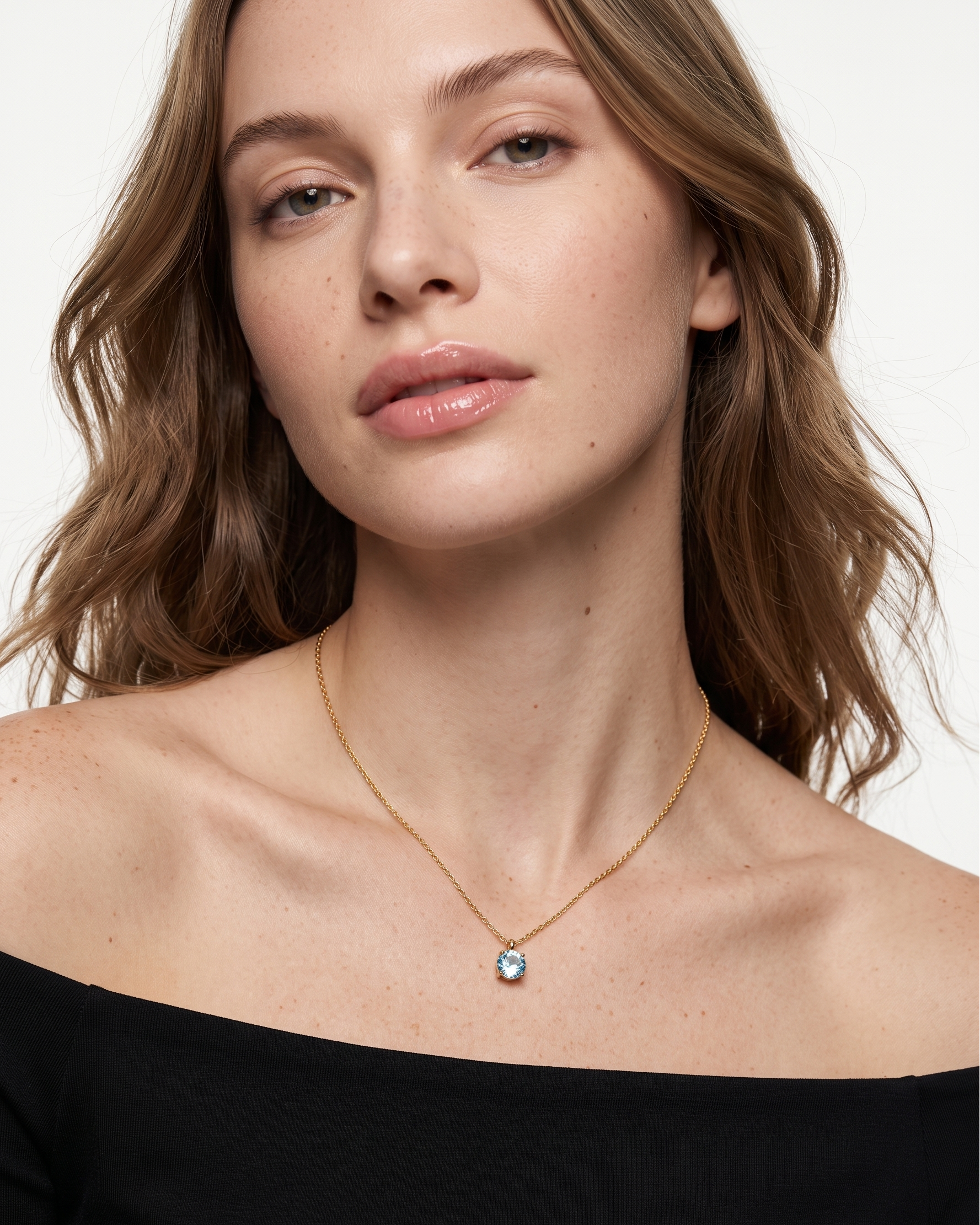 Woman wearing a necklace with a blue pendant on a plain background