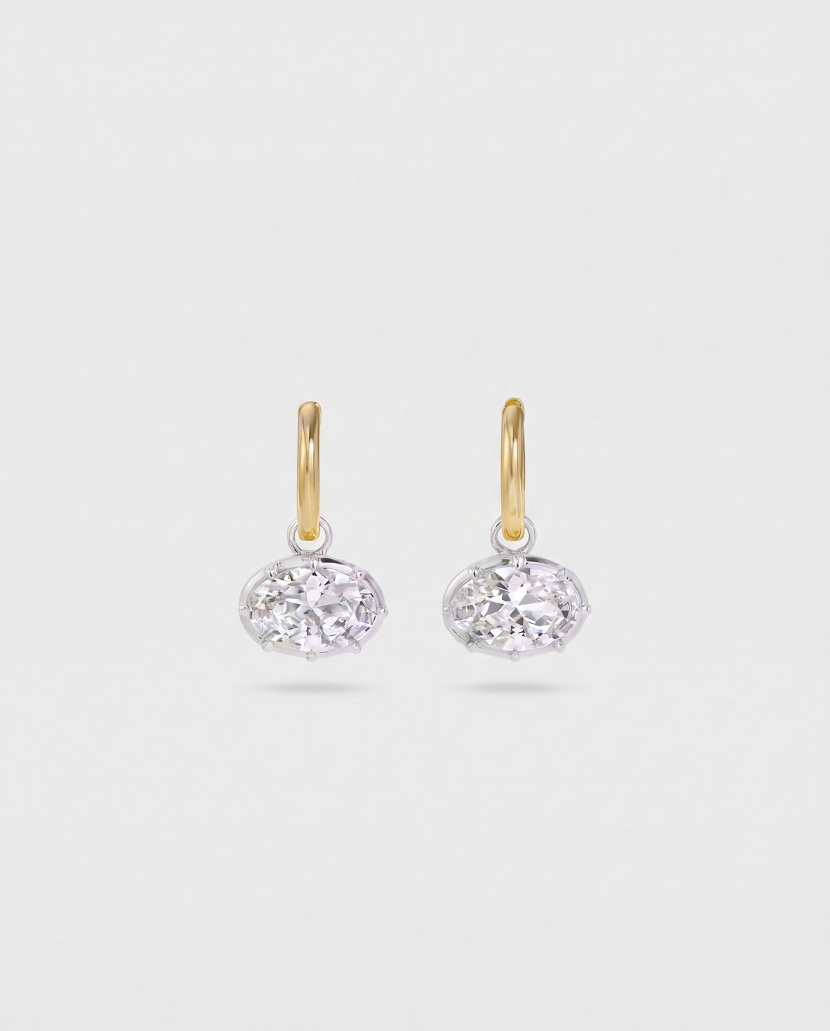 A pair of gold and silver drop earrings with oval-cut clear gemstones, displayed on a light gray background.