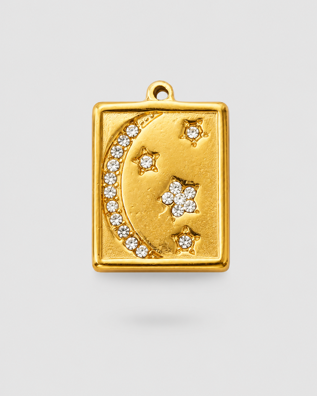 A gold-toned rectangular pendant charm featuring a crescent moon and stars, embellished with small clear stones, shown on a light gray background.
