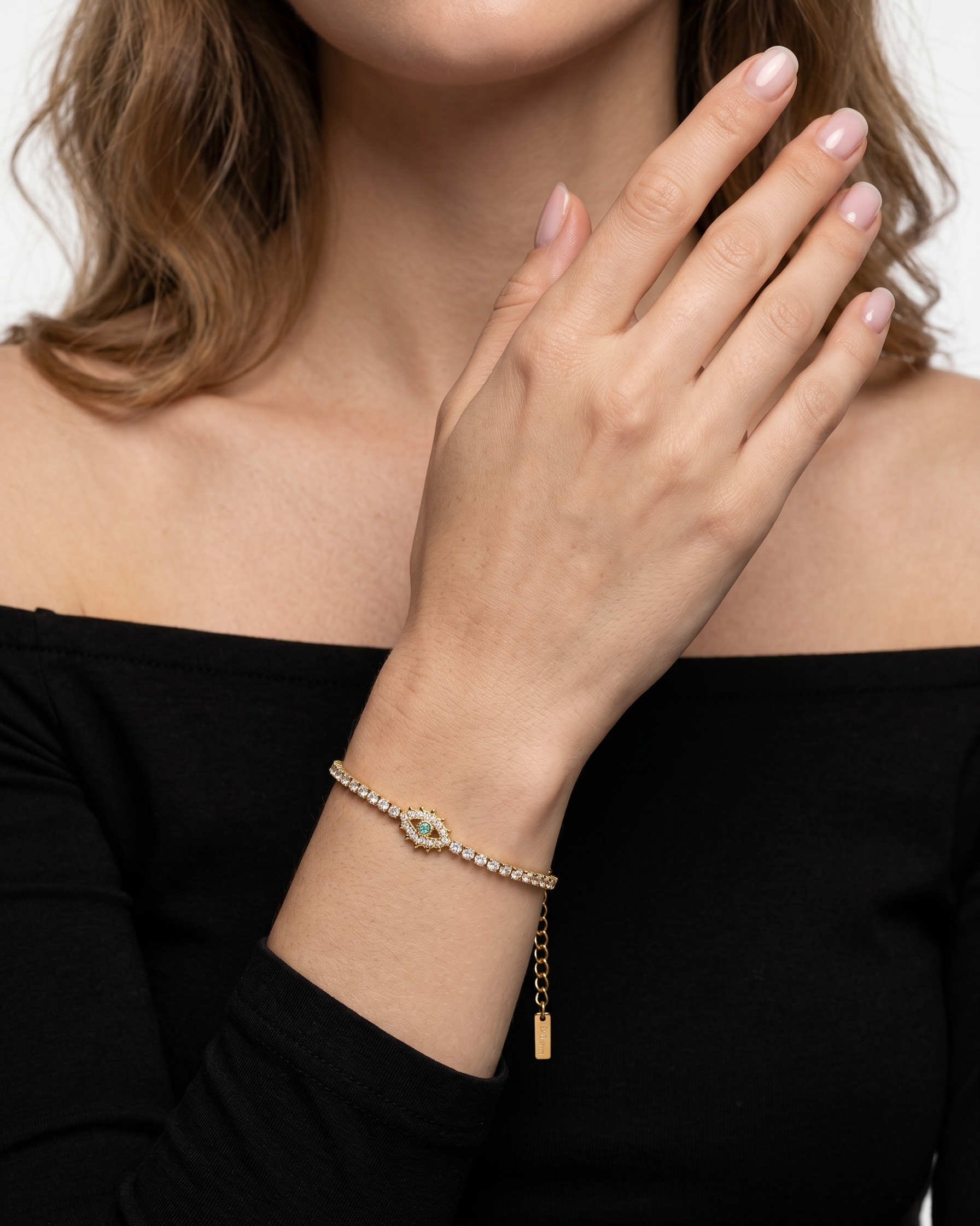 Woman wearing a gold bracelet with a green gemstone on a black top.