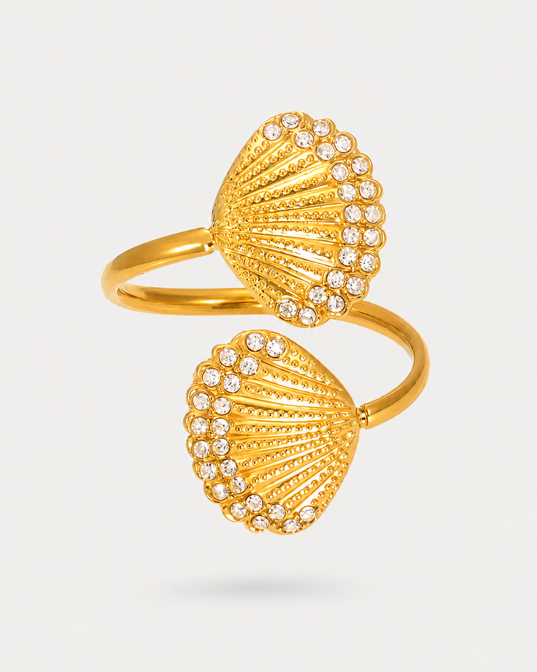 A gold-plated open ring featuring two fan-shaped shell motifs, each adorned with small clear crystals, set against a light gray background.
