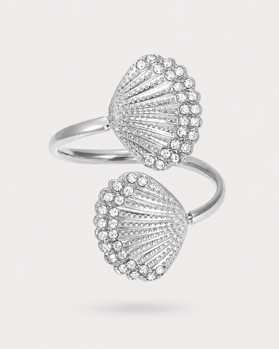 A silver-toned open ring featuring two shell-shaped clusters set with clear pavé stones, photographed on a light gray background.