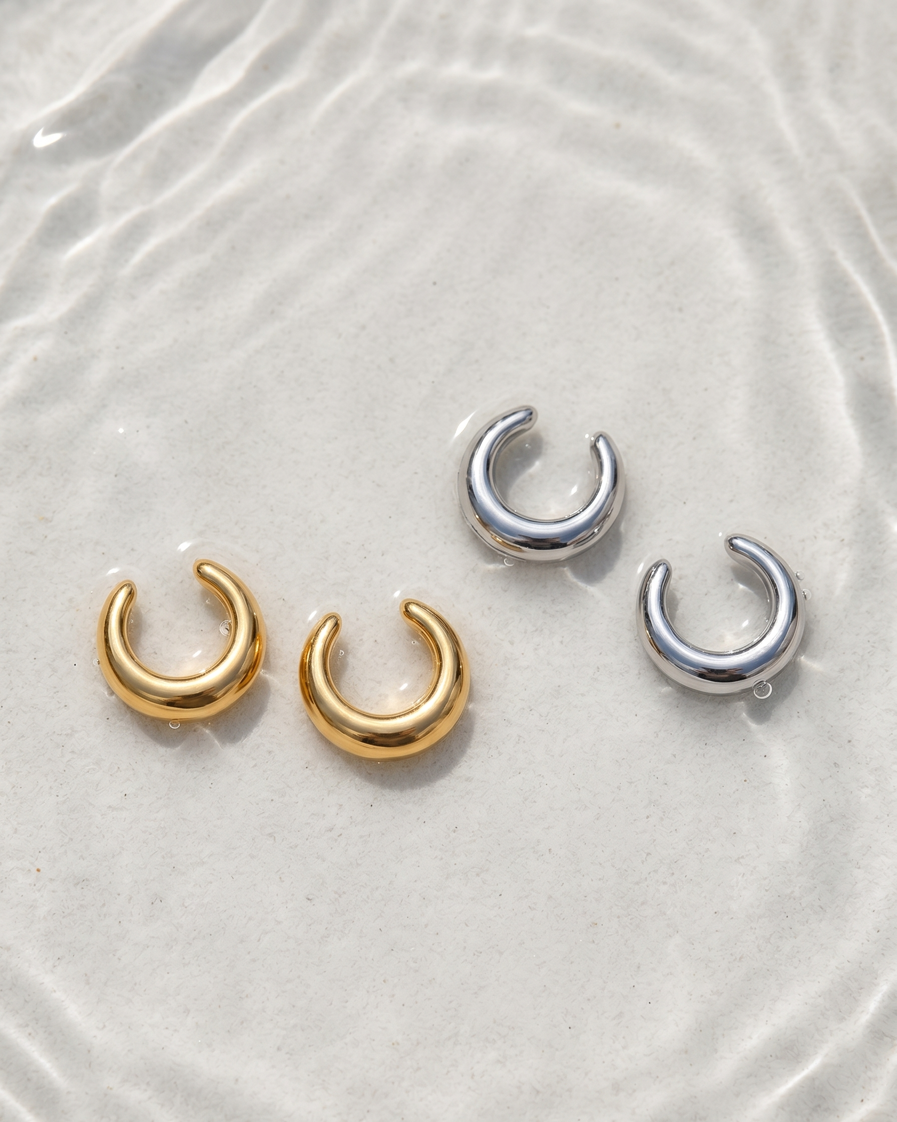 Pair of gold and silver crescent moon earrings on a textured white surface