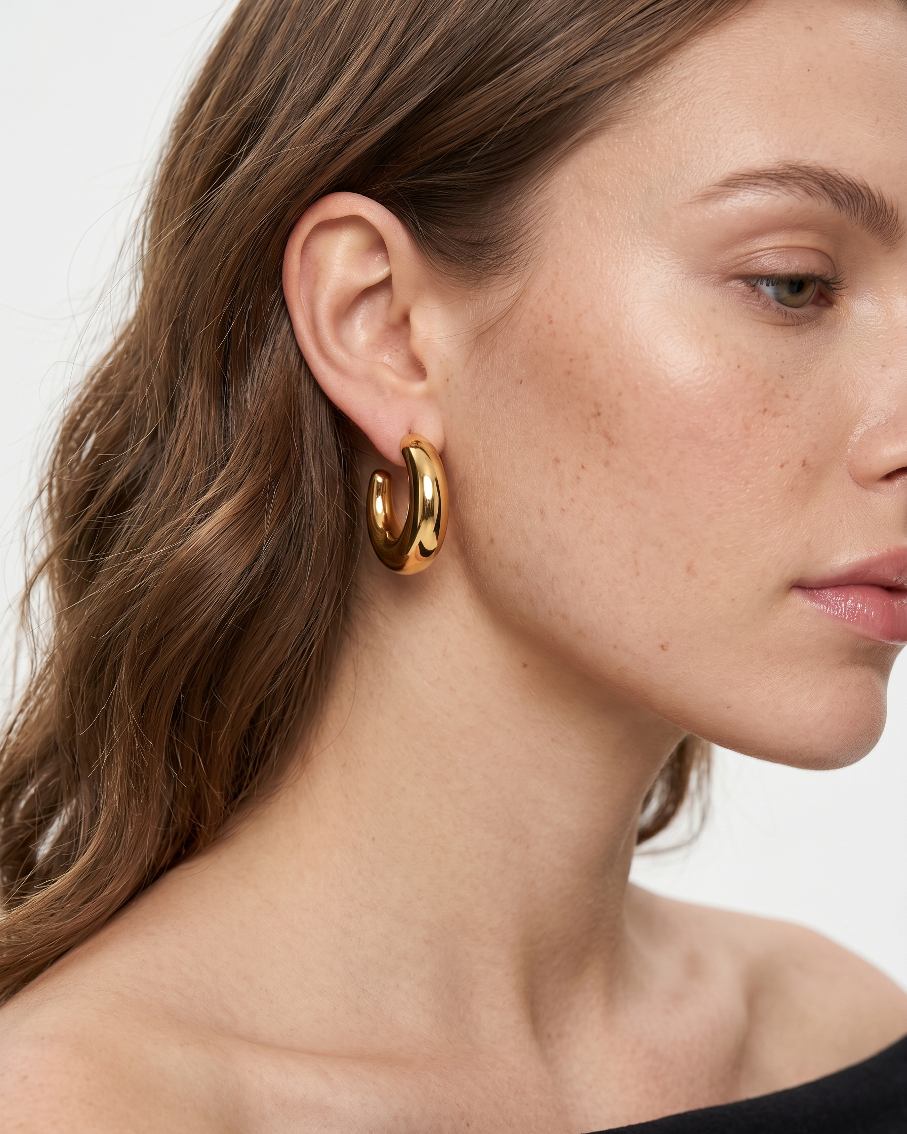 Close-up of a woman wearing gold hoop earrings with a neutral background