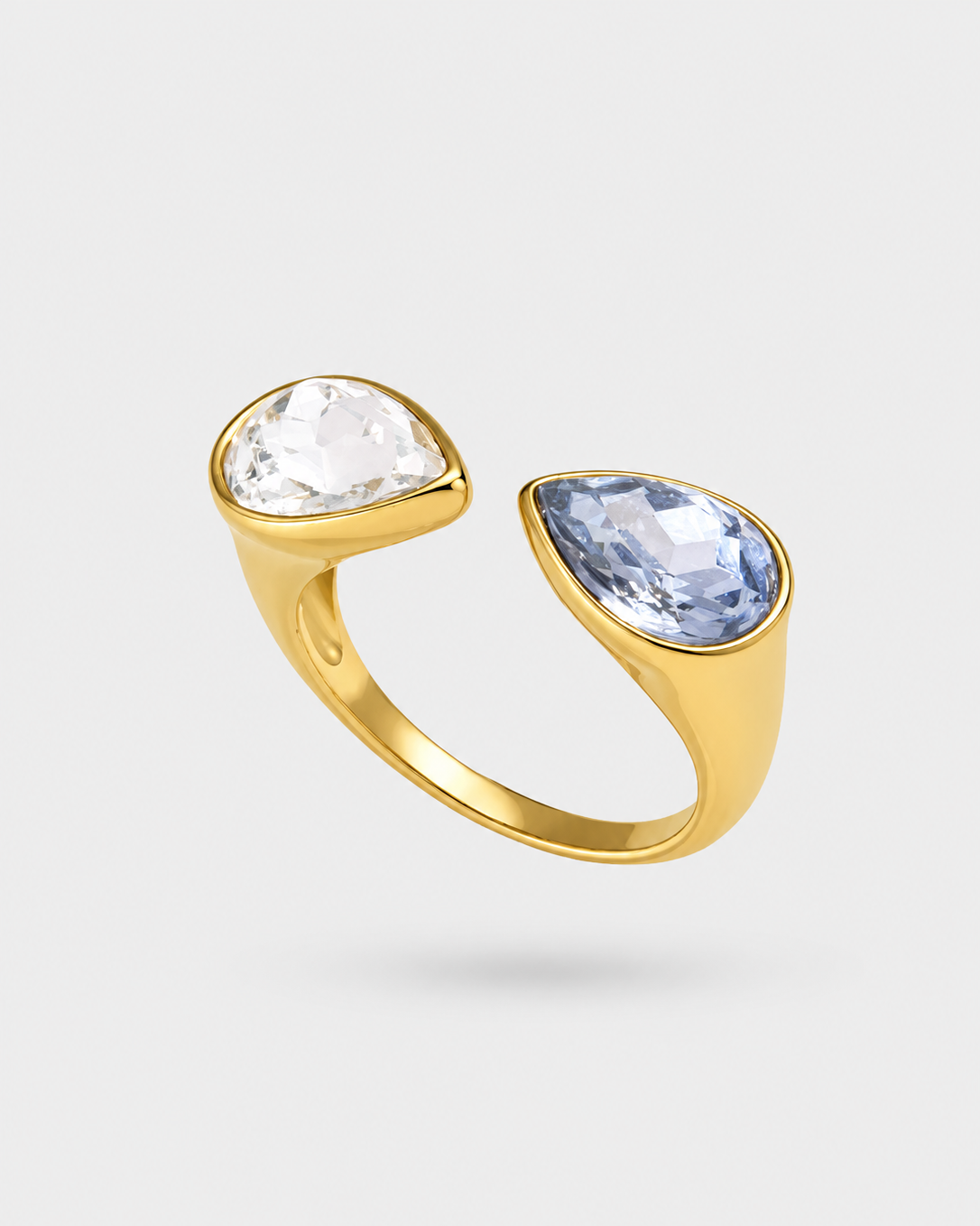 A gold open ring featuring a clear pear-cut gemstone on one side and a light blue pear-cut gemstone on the other, set against a light gray background.