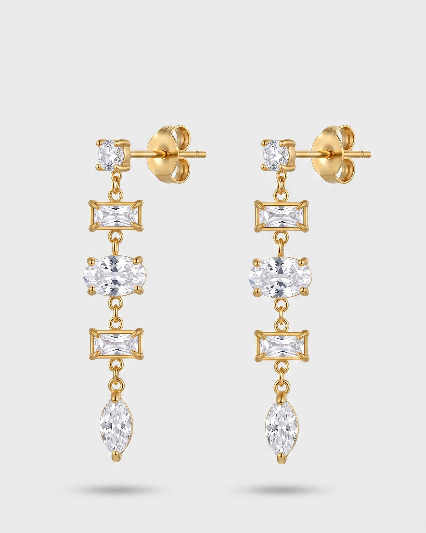 Gold earrings with clear gemstones on a light gray background