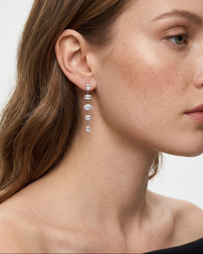Close-up of a woman wearing a dangling earring with a neutral background