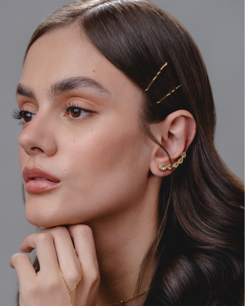 Woman wearing gold hairpins and earrings against a neutral background