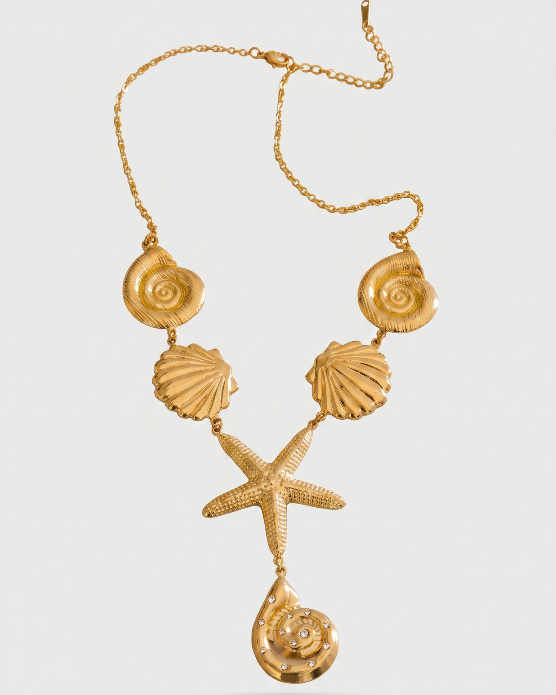 Gold necklace with shell and starfish pendants on a light gray background