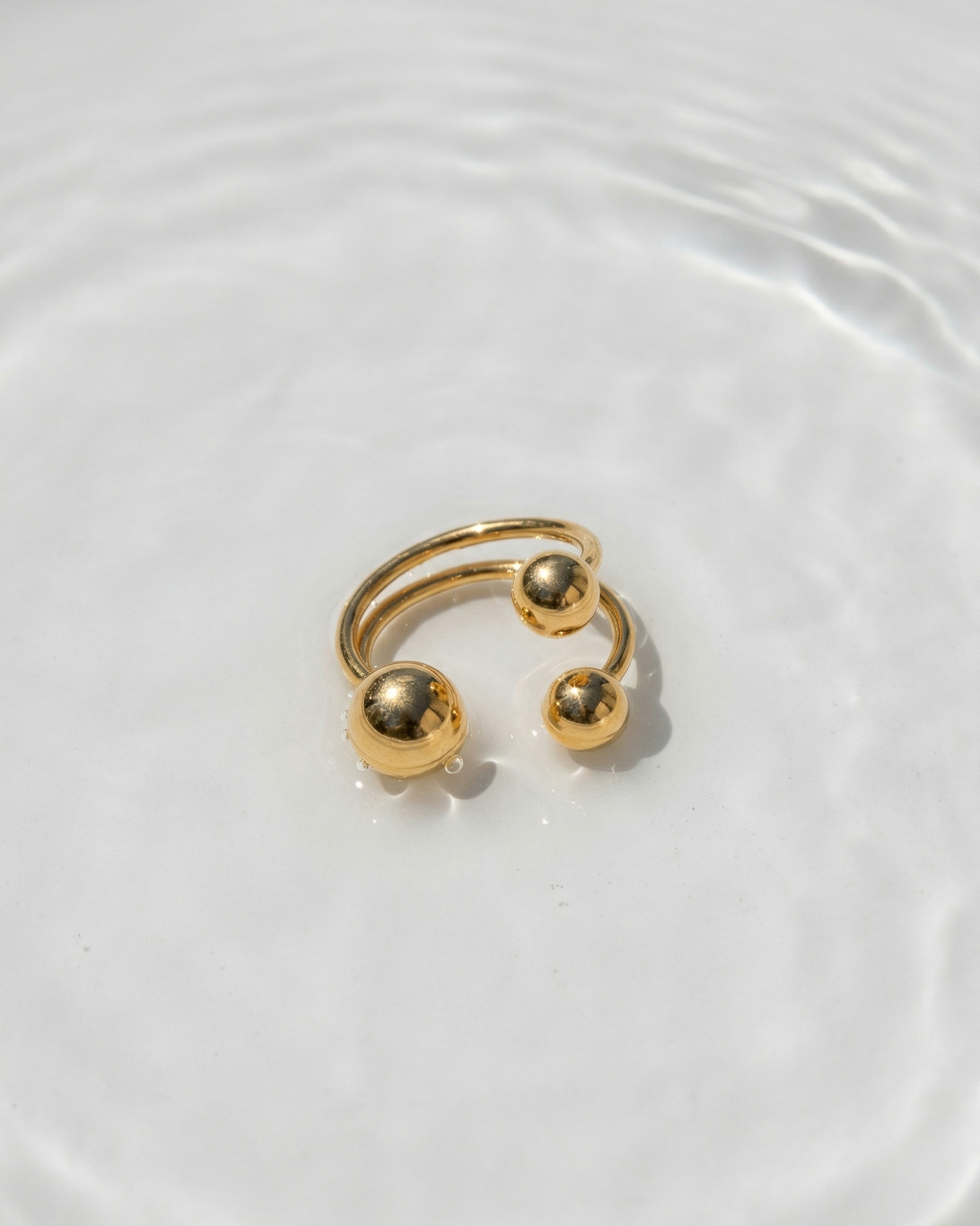Gold open ring with spherical ends on a white background