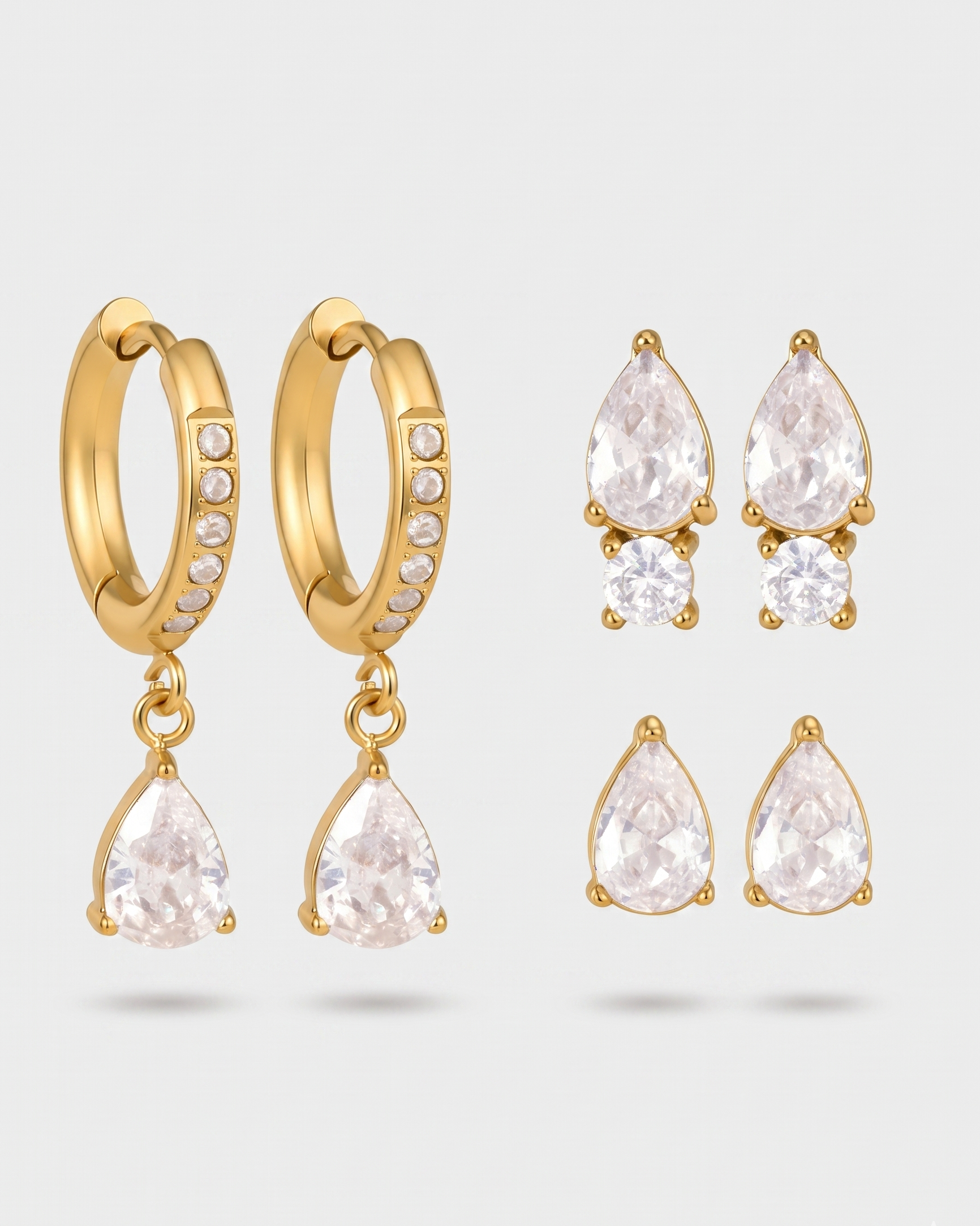 Gold hoop earrings with teardrop-shaped crystal drops on a light gray background