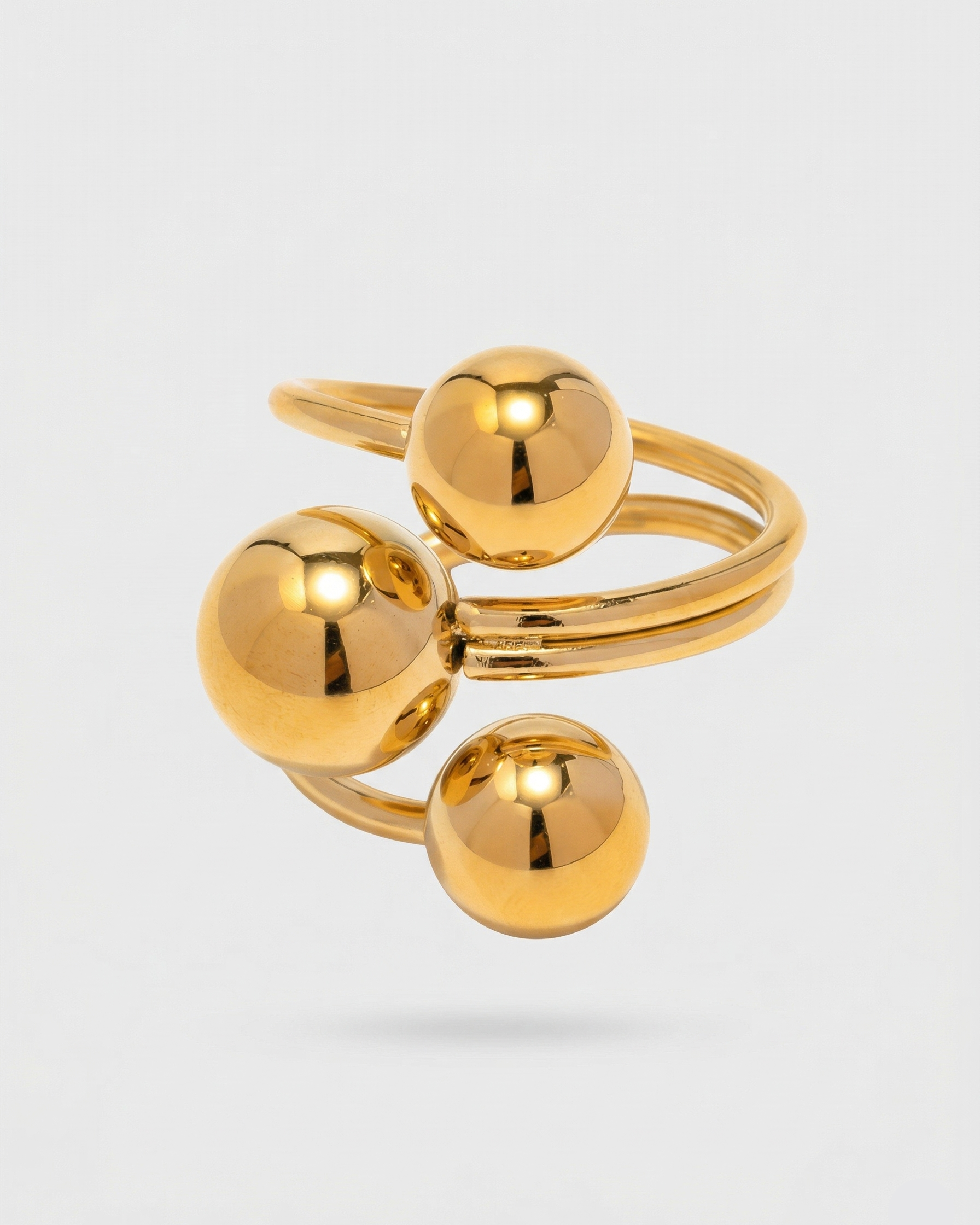 Gold ring with three spherical components on a light gray background