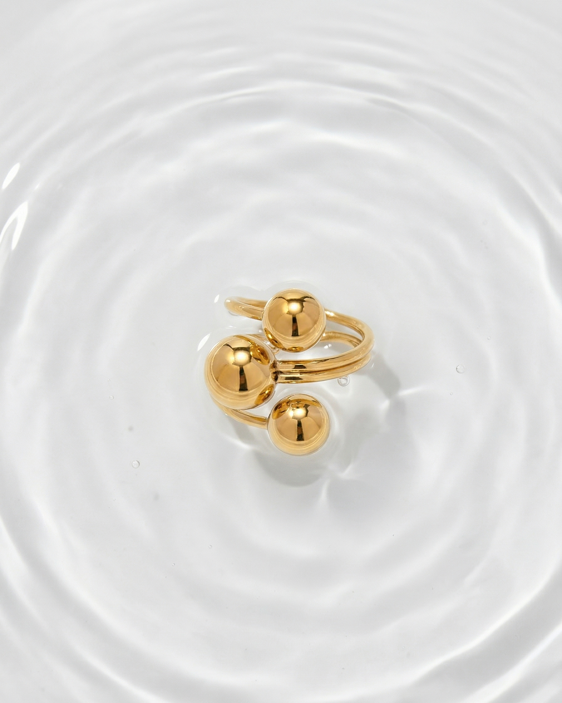 Gold ring with three spherical elements on a white surface