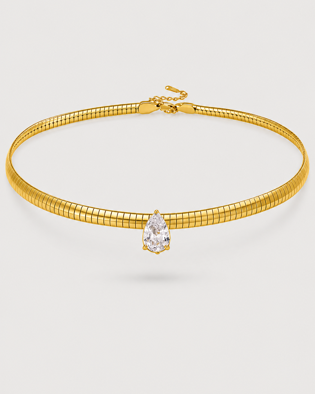 A gold snake chain choker necklace featuring a single pear-cut clear gemstone in a gold bezel setting, displayed on a light gray background.