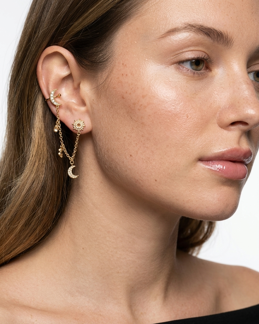 Close-up of a woman wearing a gold earring with charms on a white background