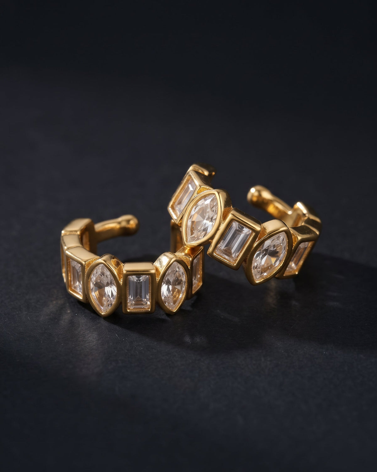 Gold-toned stretch ring with clear baguette and marquise-cut stones, photographed on a dark black background.
