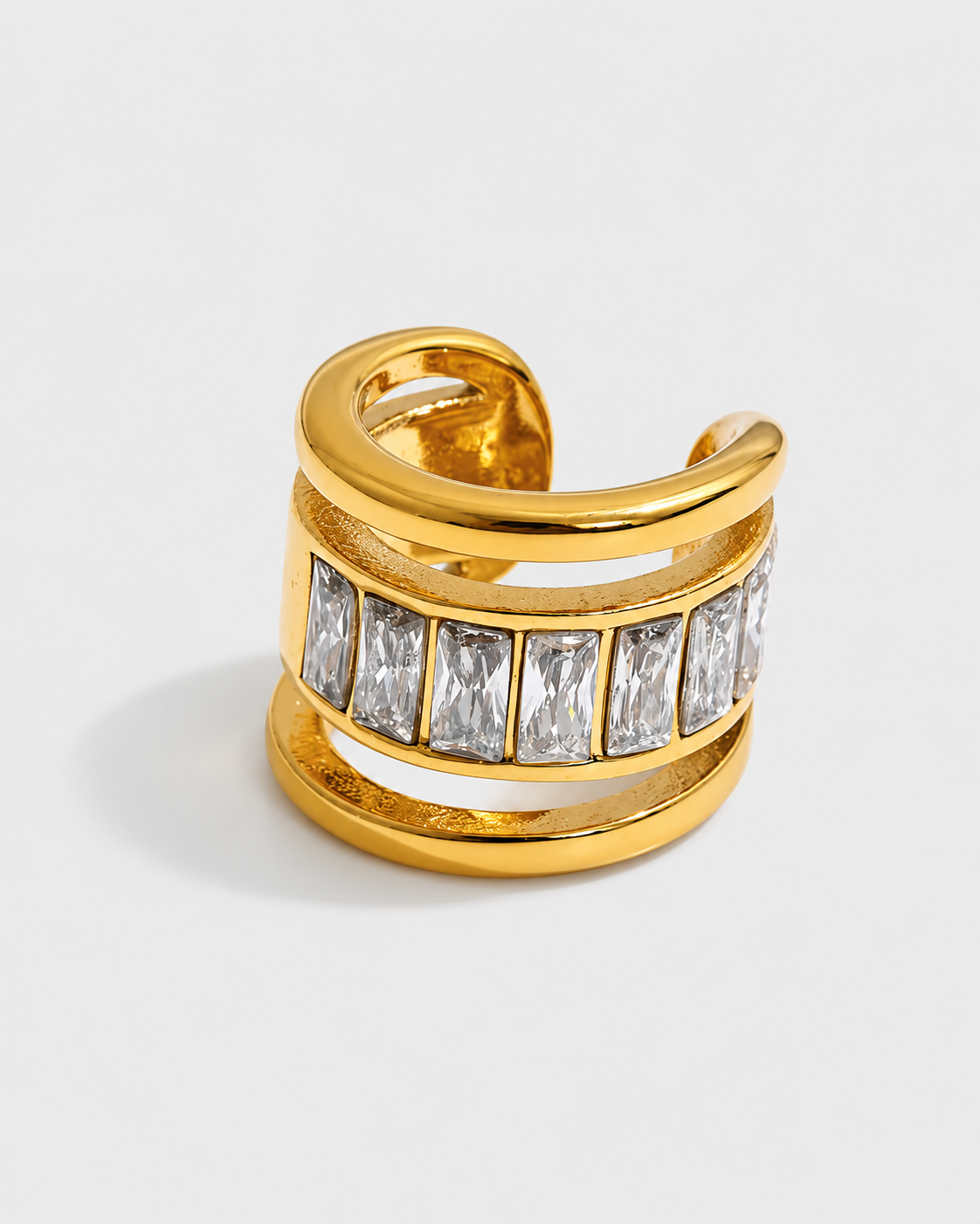 A gold-toned wrap ring featuring a row of clear rectangular baguette gemstones, photographed on a light gray background.