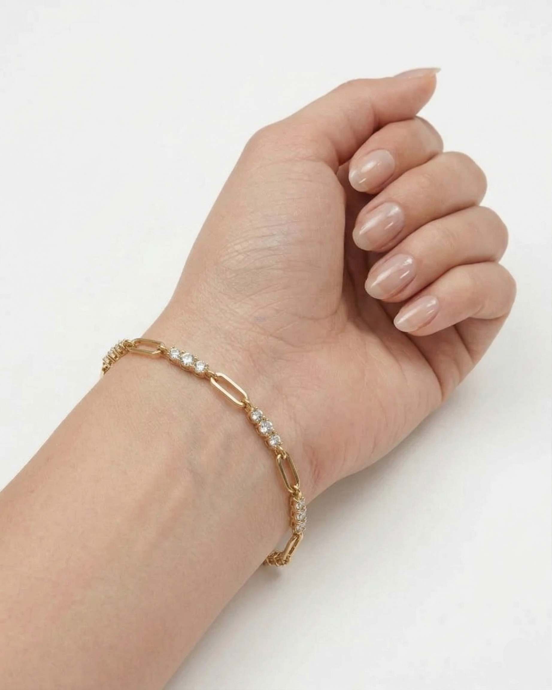Gold bracelet with small stones on a wrist against a white background