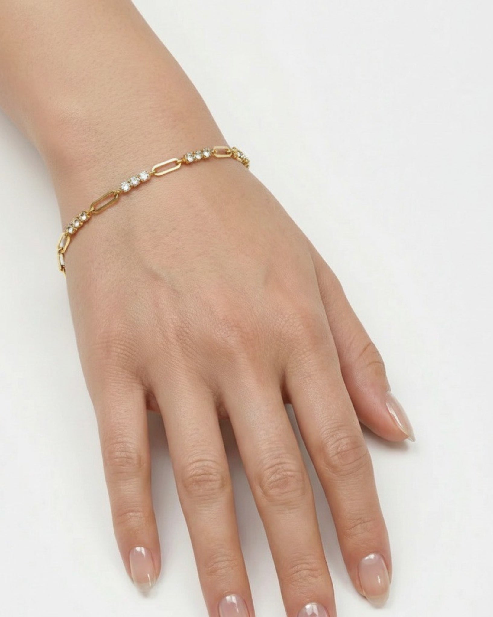 Hand wearing a gold bracelet with pearls on a white background