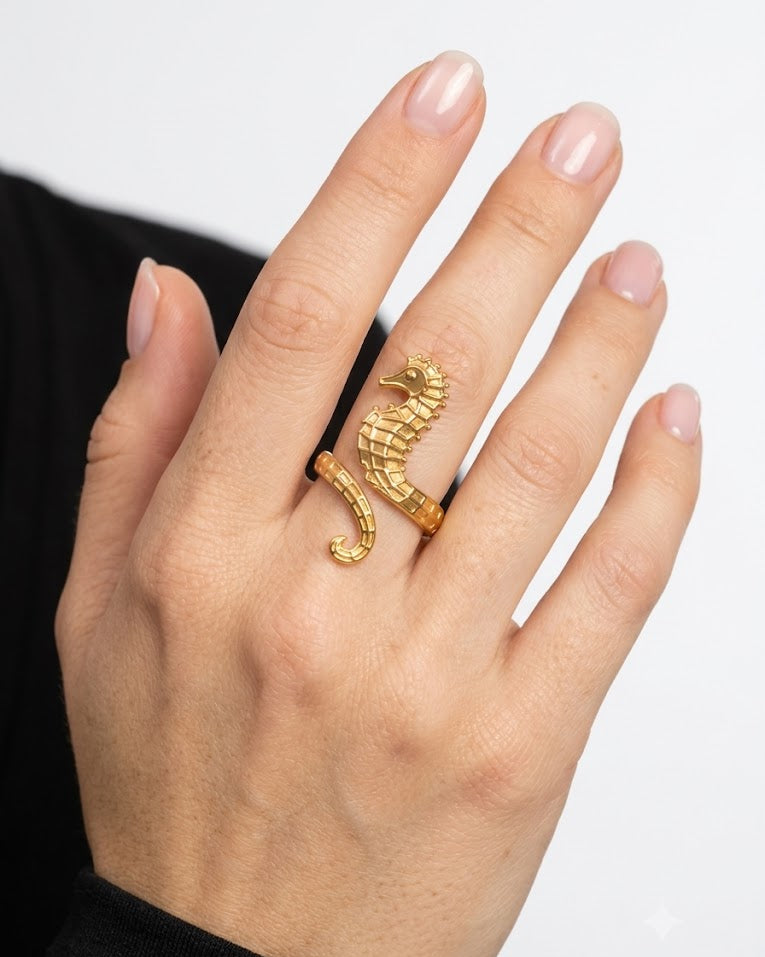 Hand wearing a gold scorpion ring on a plain background