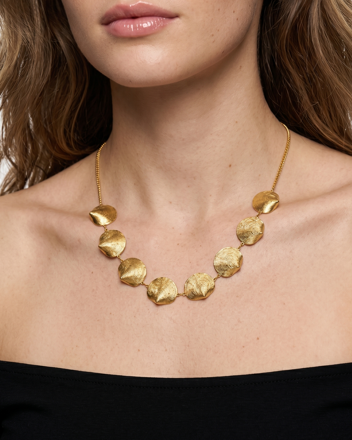 Woman wearing a gold necklace against a white background