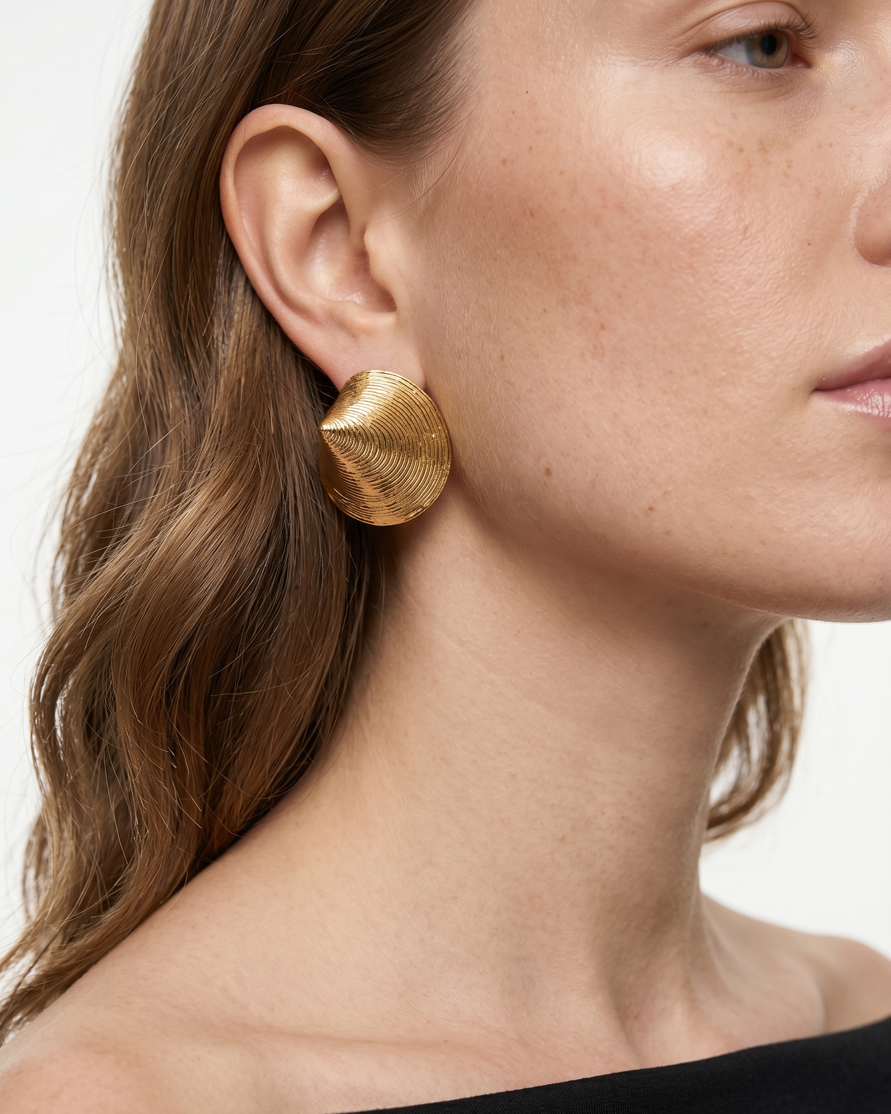 Close-up of a person wearing gold earrings with a neutral background