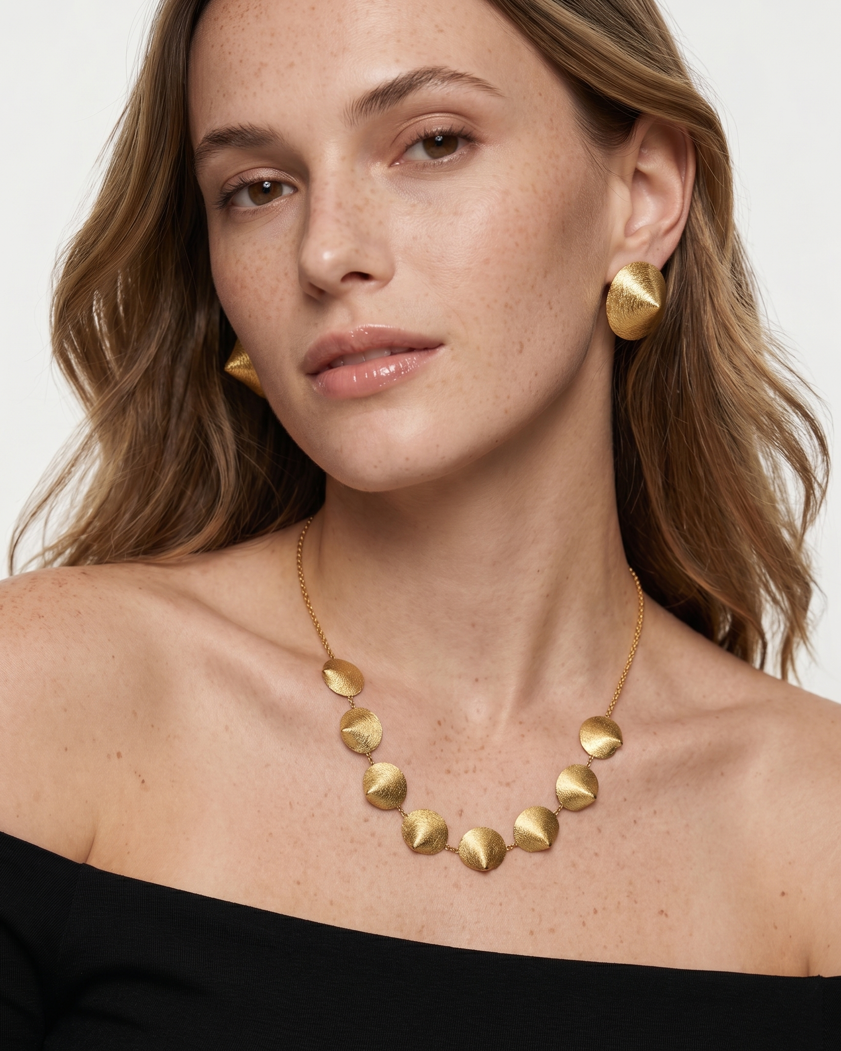Woman wearing a gold necklace and earrings on a plain background