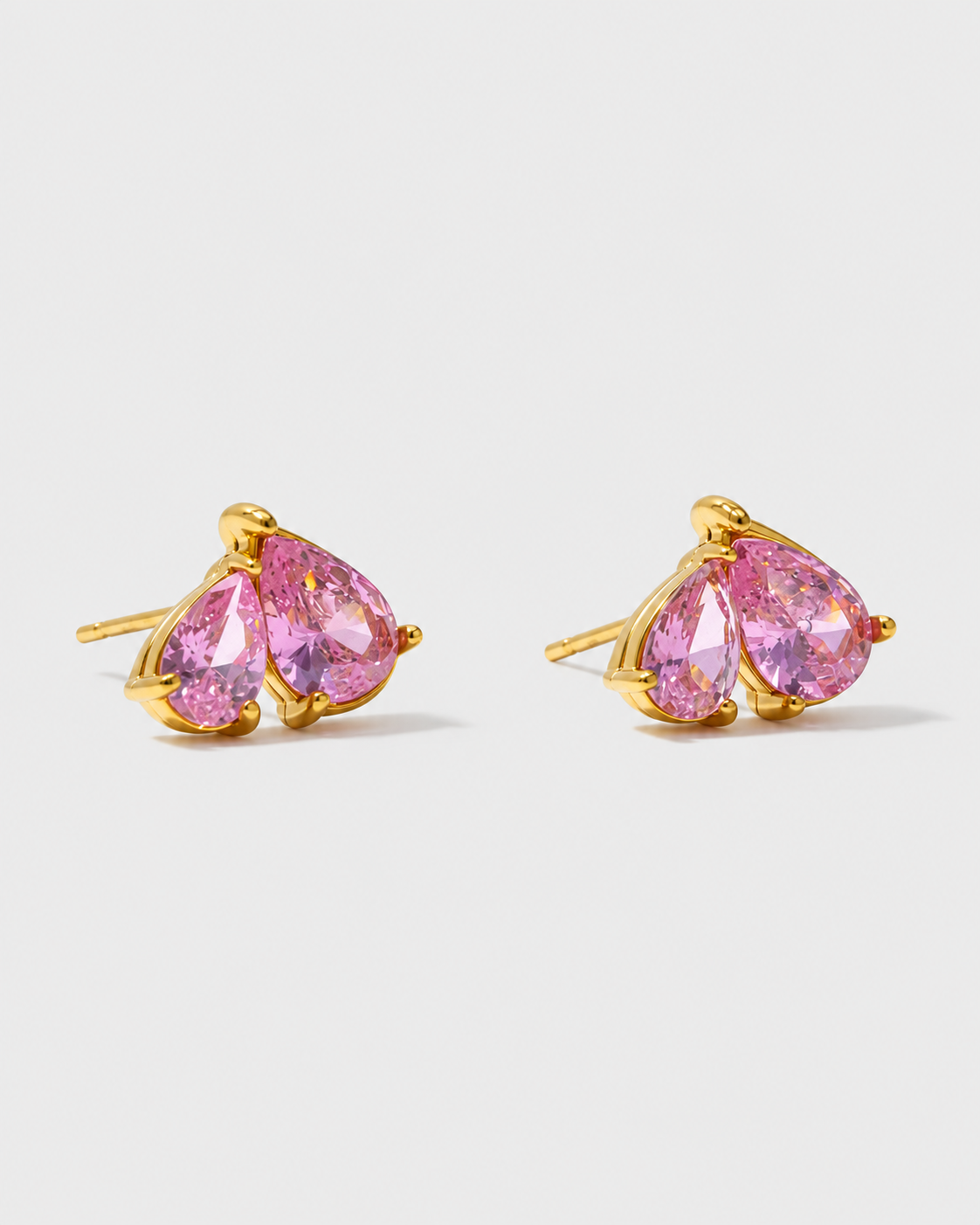 A pair of gold stud earrings featuring pear-cut pink gemstones in a prong setting, shown against a light gray background.