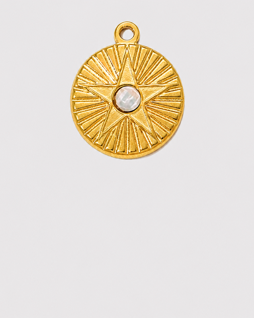 A round gold-toned pendant charm featuring a textured sunburst design and a central white pearl, shown on a solid light gray background.