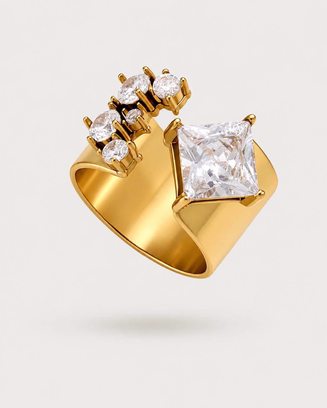 A gold ring featuring a large princess-cut clear gemstone and three smaller round clear gemstones set in a curved gold band, shown on a light gray background.