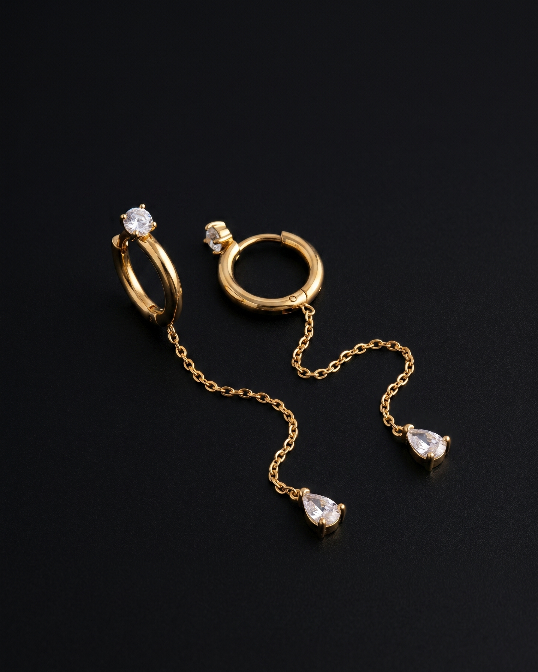 Gold hoop earrings with chain and teardrop-shaped gemstones on a black background