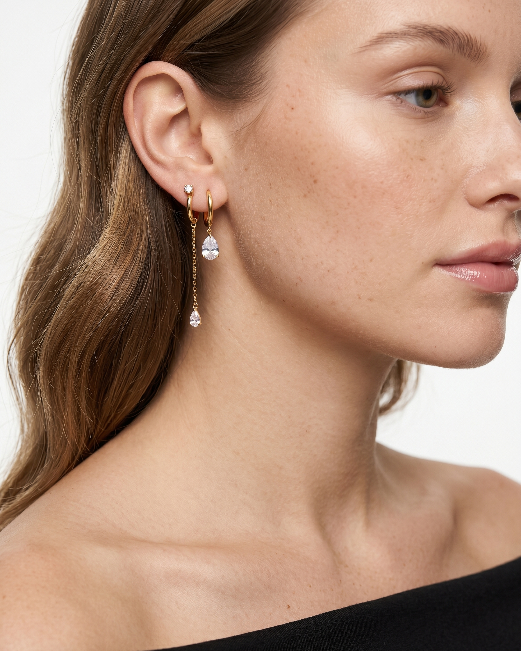 Close-up of a woman wearing gold hoop earrings with clear gemstones on a white background
