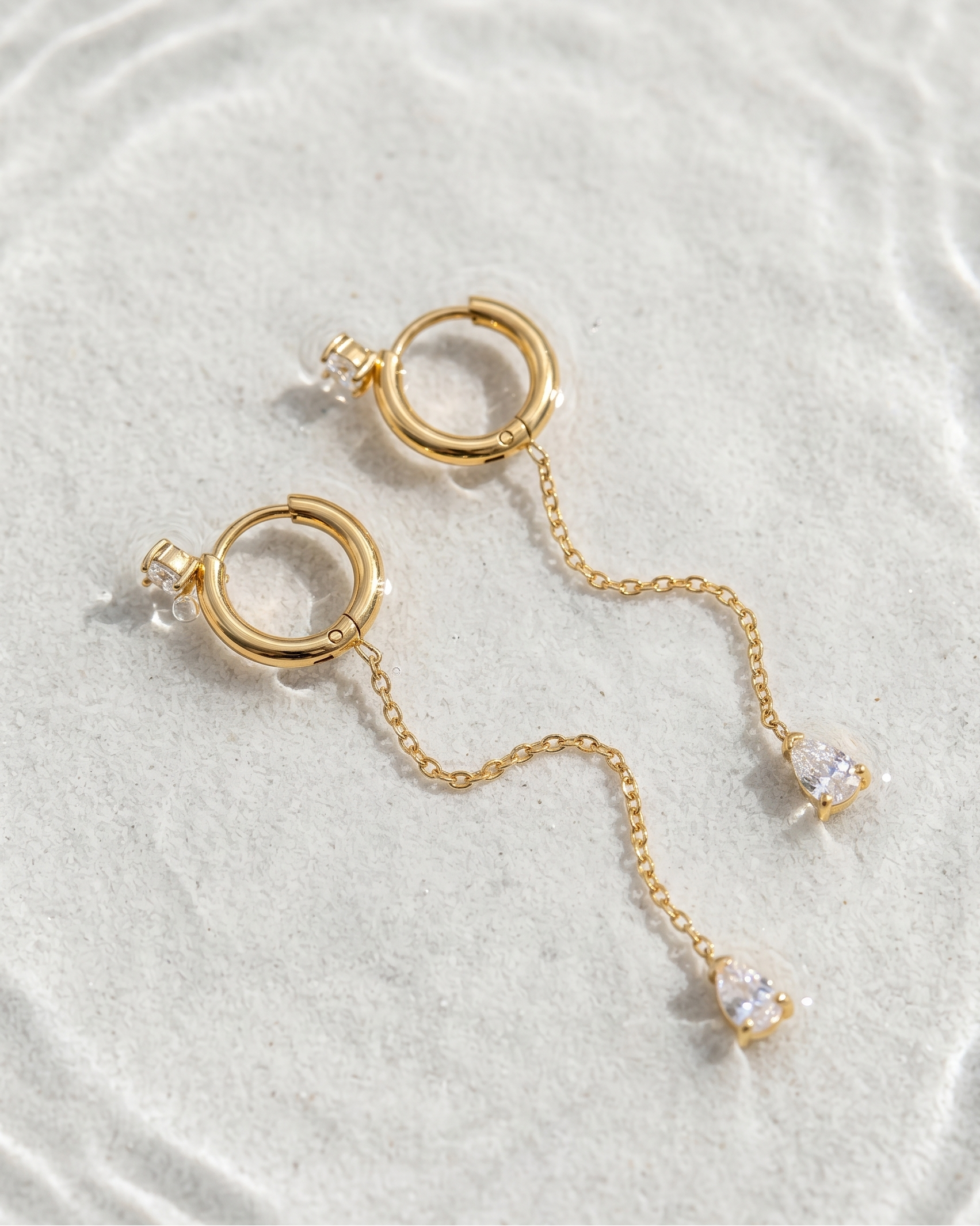 Gold earrings with chain and clear stones on a light gray background