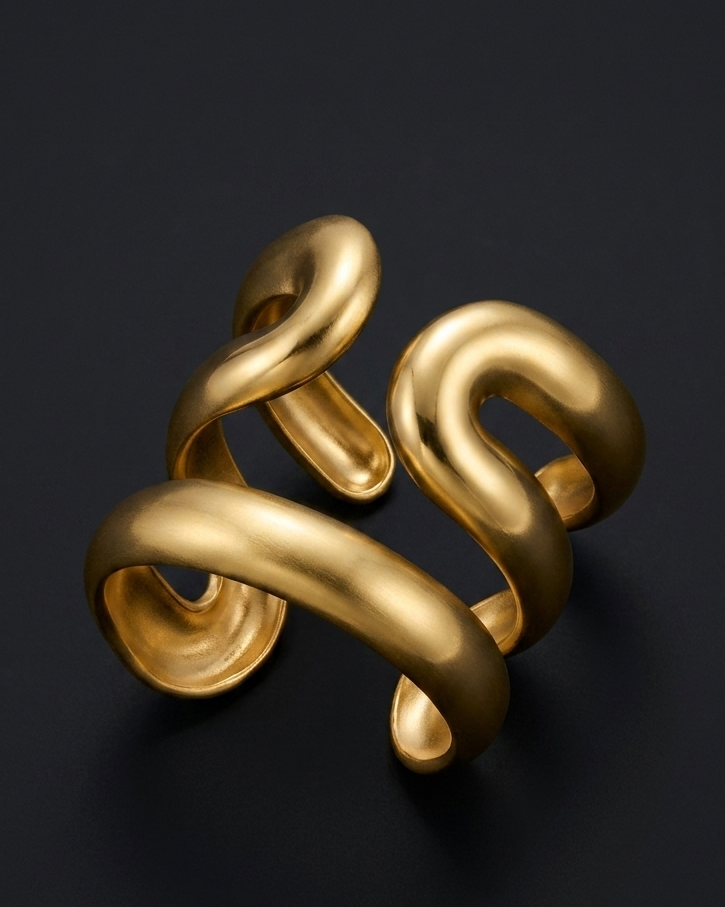 A sculptural gold ring with a twisted, fluid ribbon-like form, photographed on a dark charcoal background.