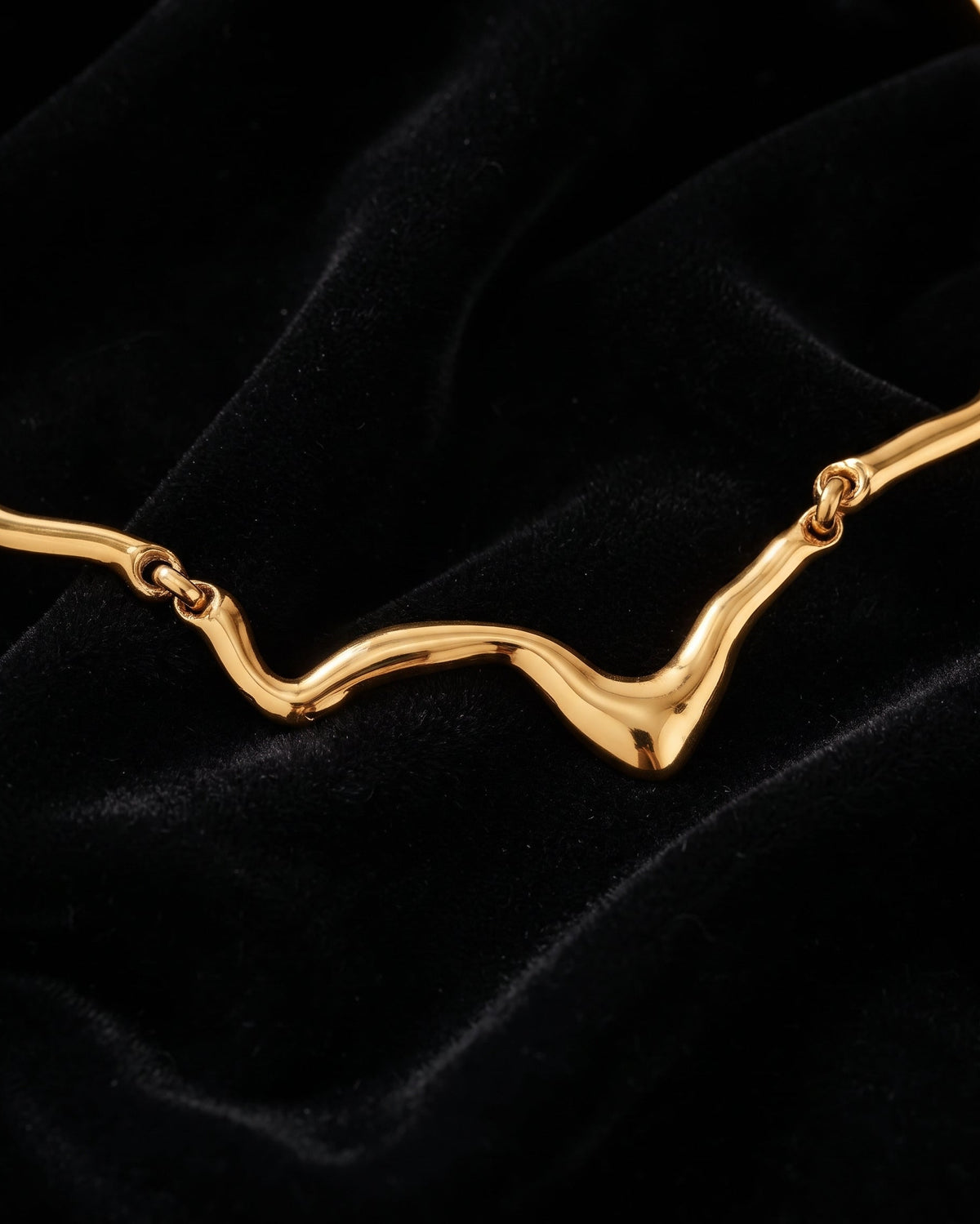 A close-up of a gold wavy chain necklace laid on a black velvet fabric background.