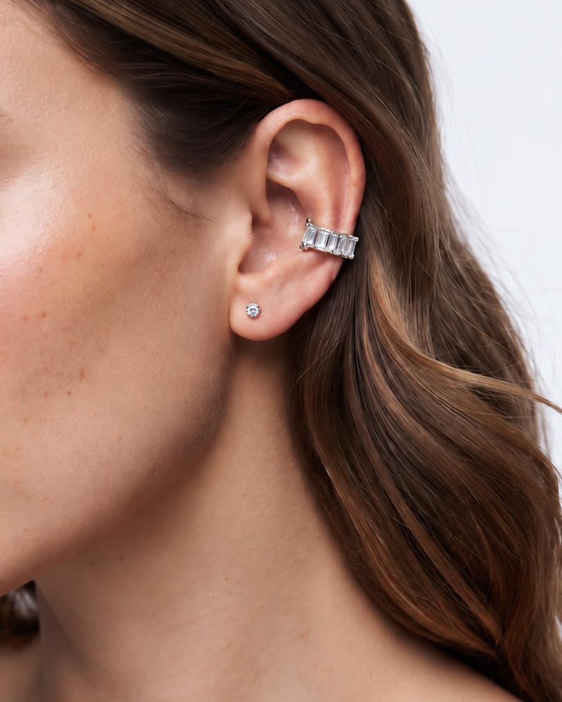 A close-up of a woman's ear wearing a silver-toned multi-stone ear cuff with a small matching stud earring, against a clean light background.