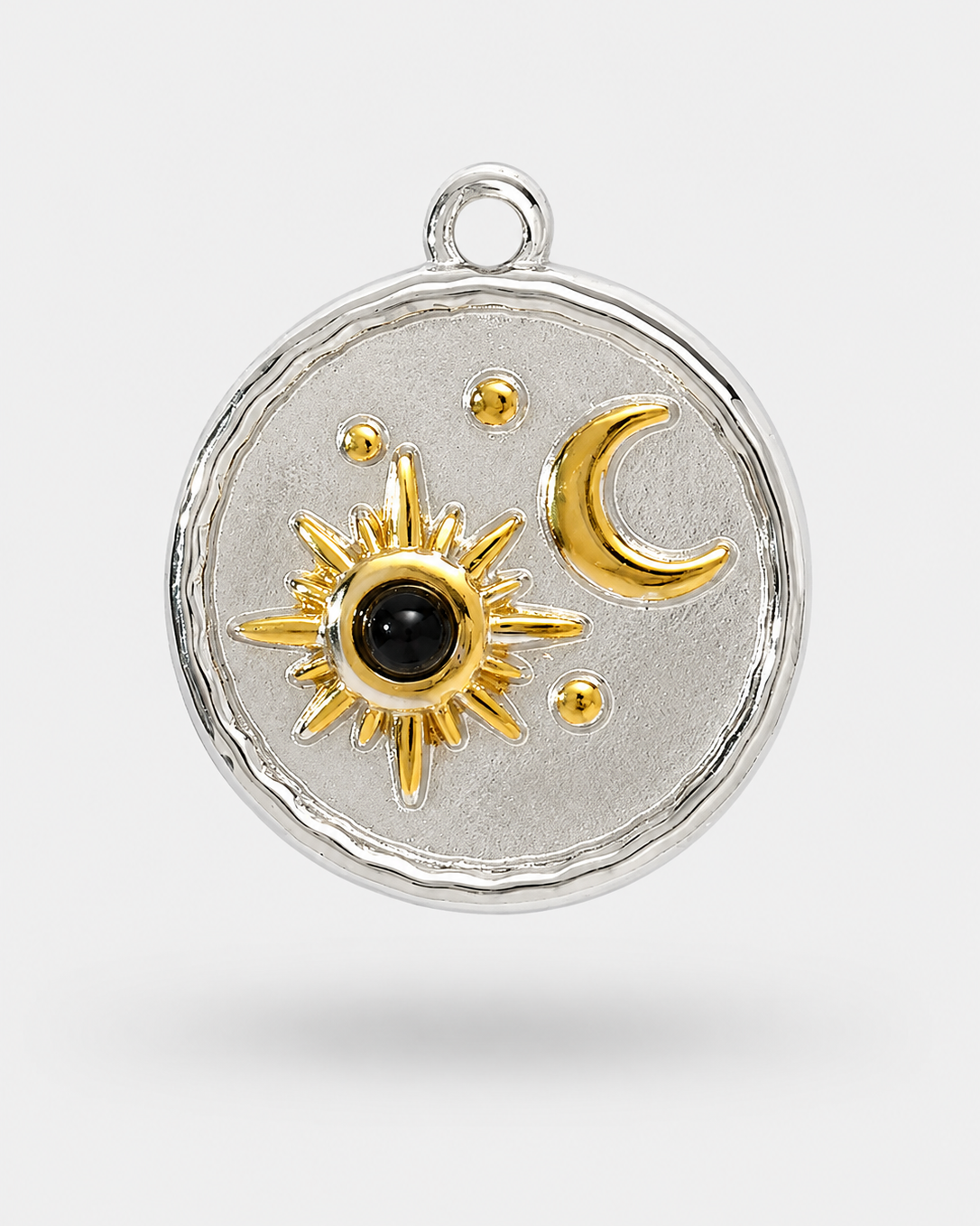A round silver pendant with a textured finish, featuring a gold sun with a black center and a gold crescent moon, on a light gray background.