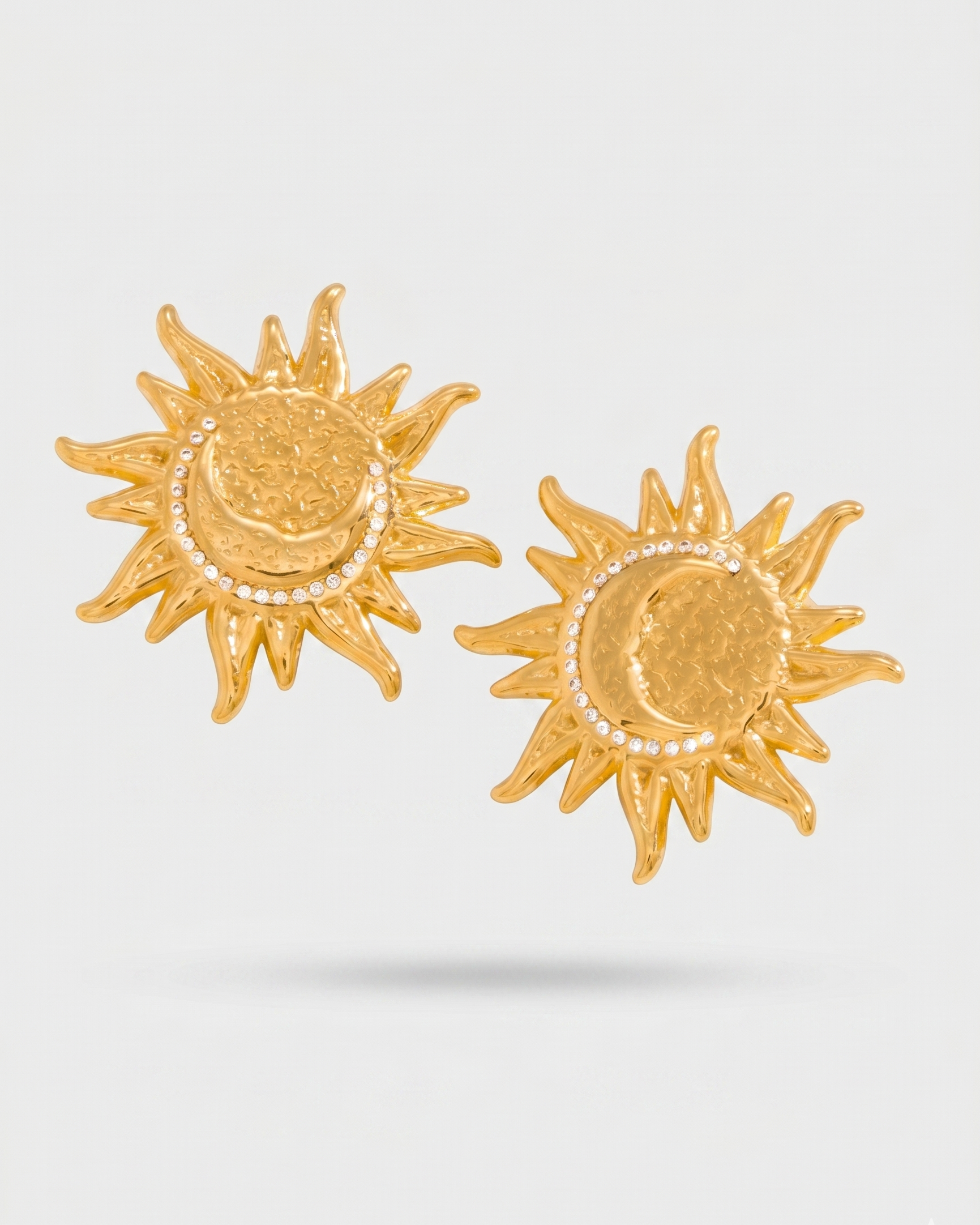 Gold sun-shaped earrings with embedded stones on a light gray background
