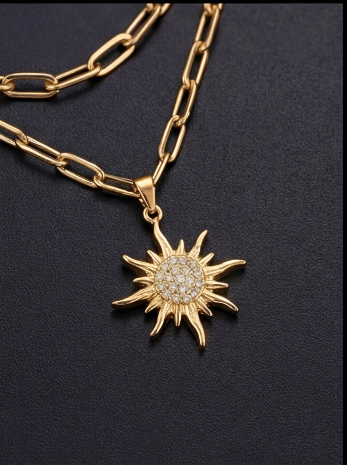 Gold chain necklace with a sun-shaped pendant on a black background