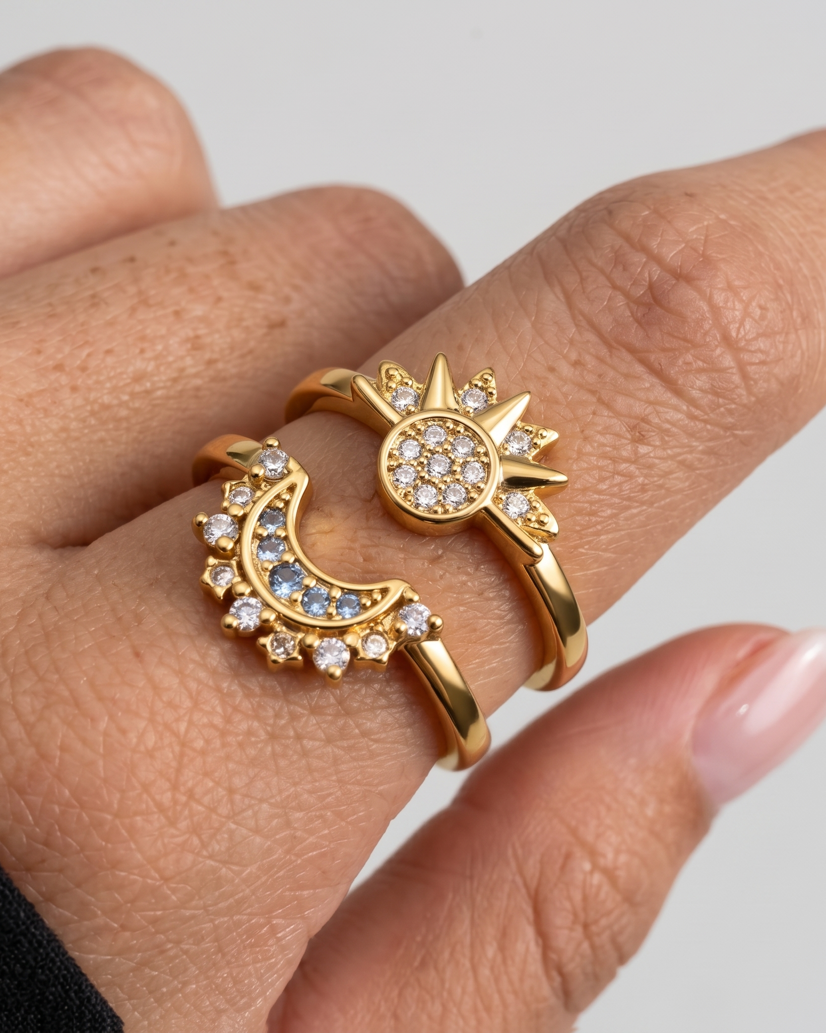 Gold ring with sun and moon design on a finger against a neutral background