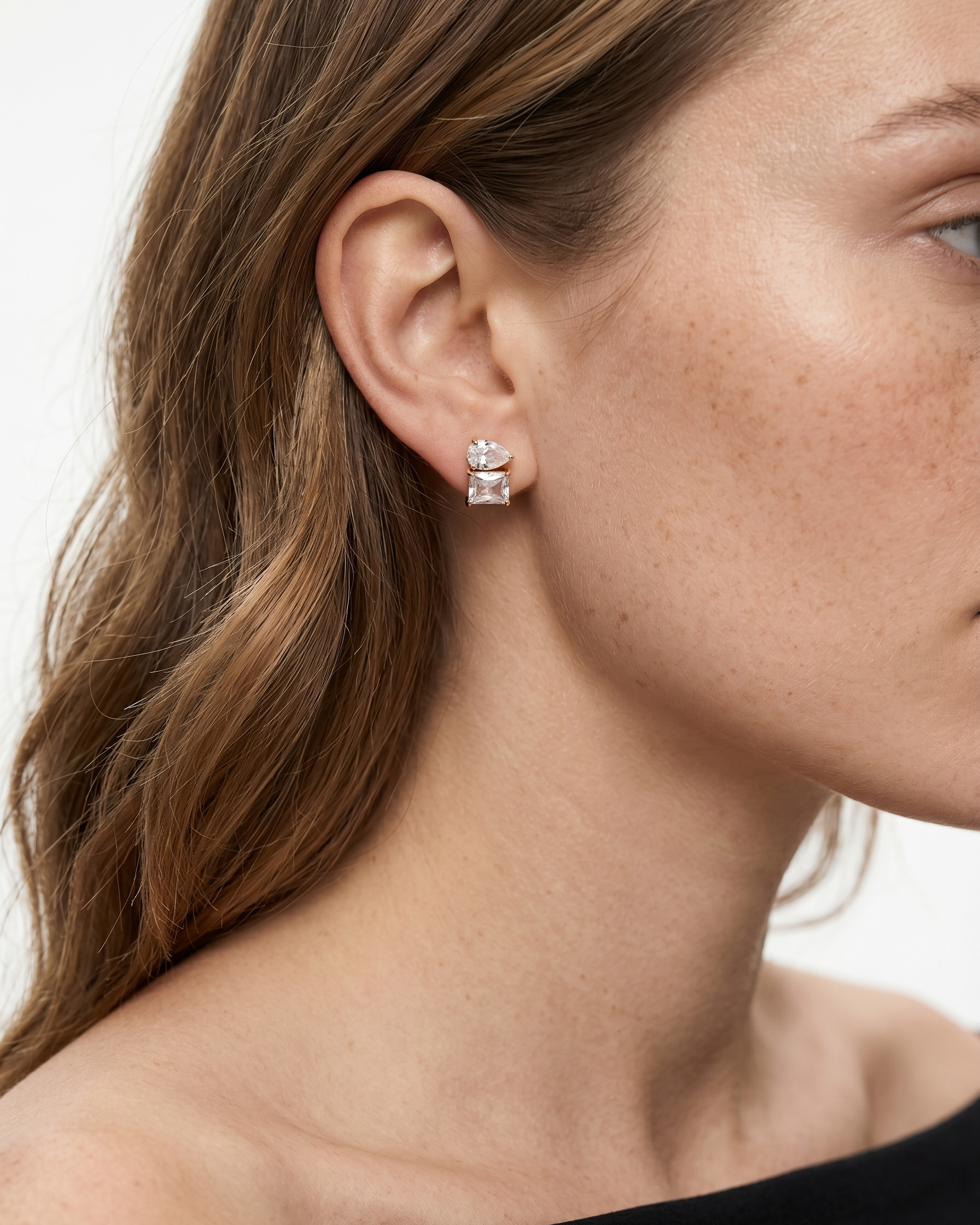 Close-up of a woman wearing diamond stud earrings with a neutral background