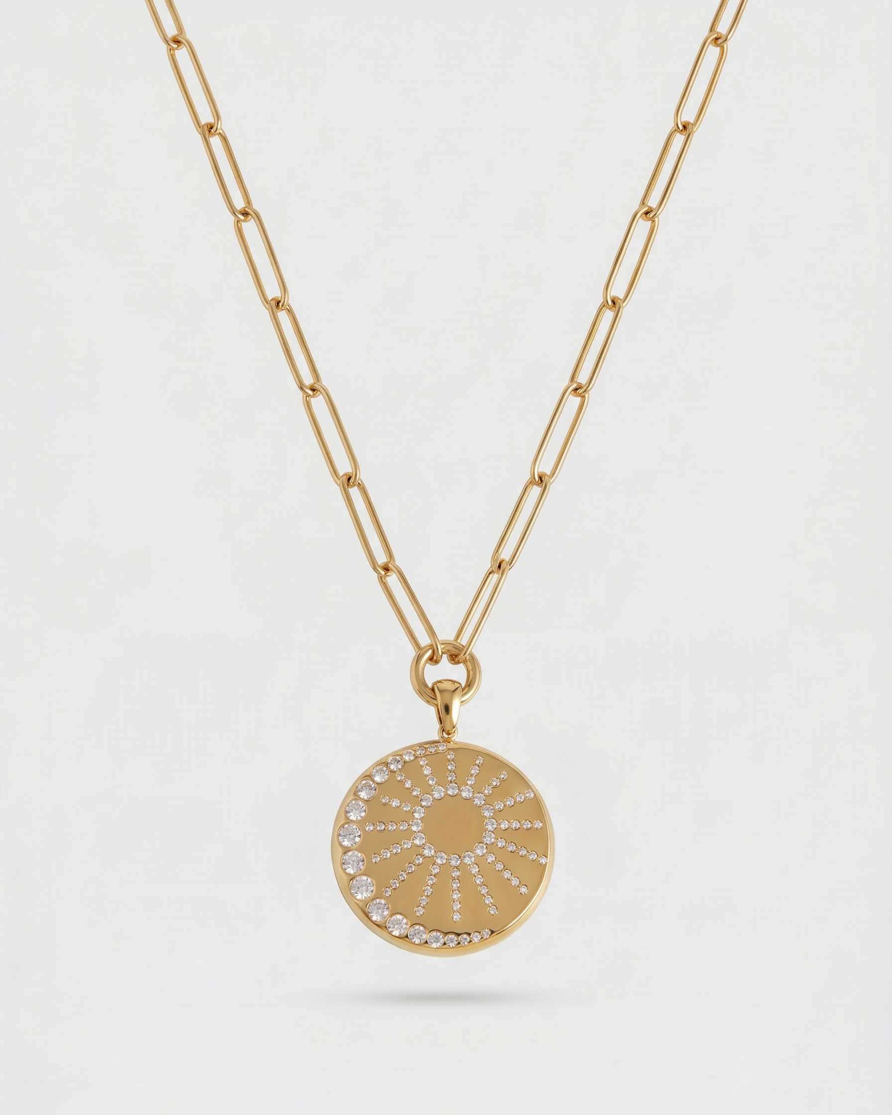 Gold necklace with a round pendant on a light gray background