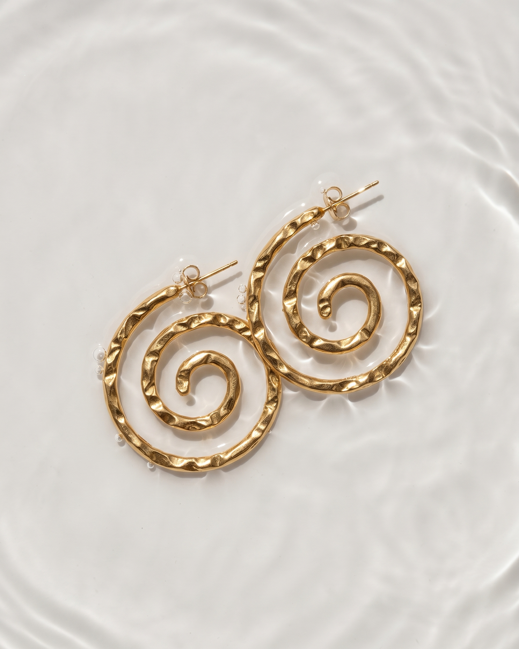 Gold spiral earrings on a white plate