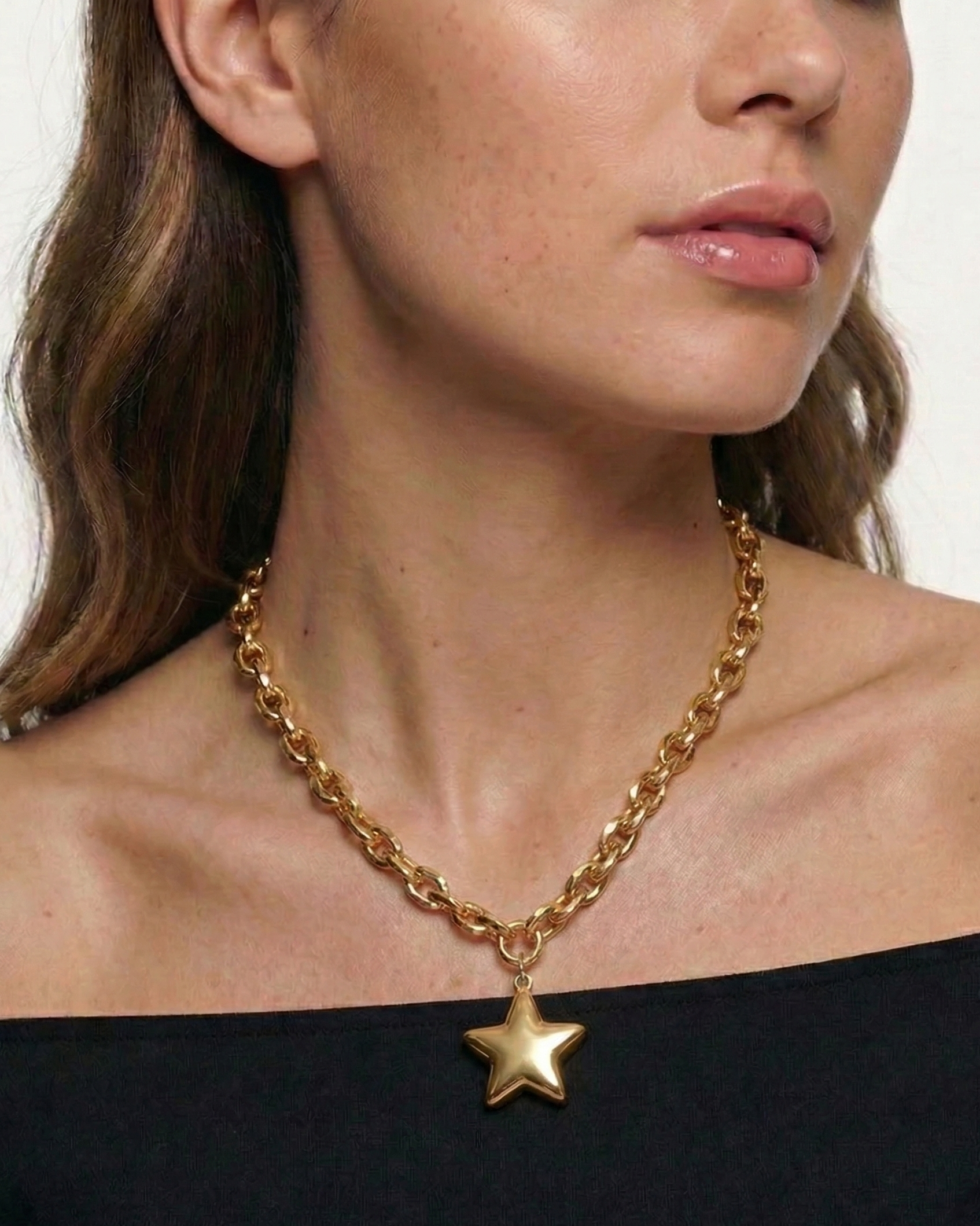 Woman wearing a gold chain necklace with a star pendant on a plain background