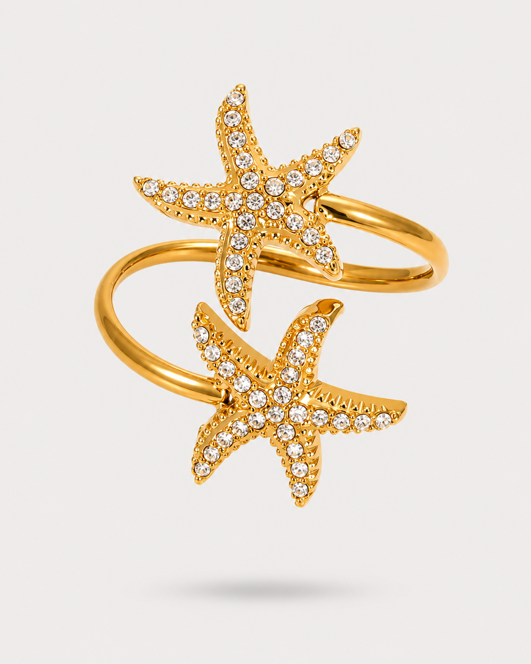 A gold wrap ring featuring two starfish motifs, each adorned with small clear pavé stones, set against a light gray background.