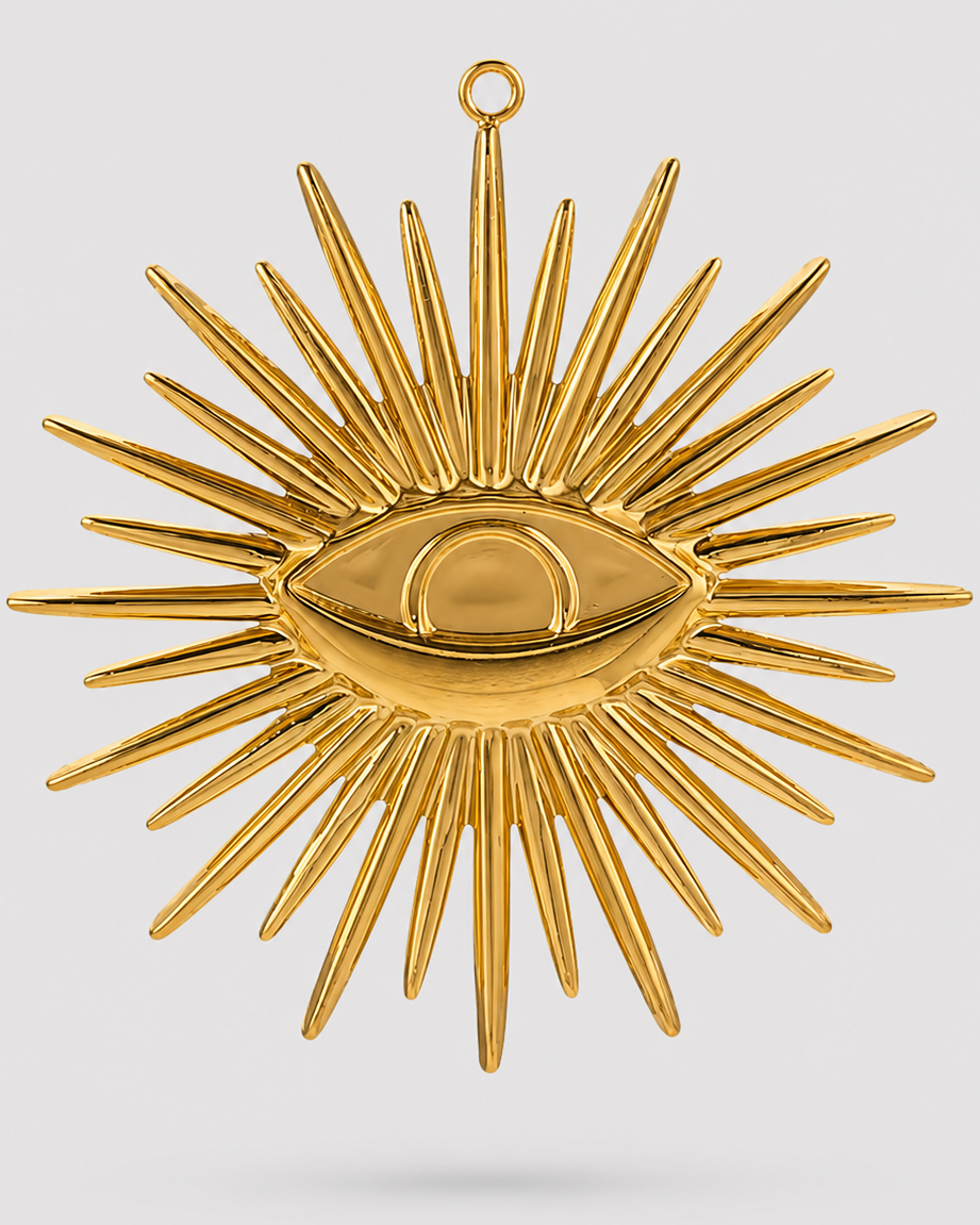 A gold-toned metal wall hanging ornament shaped like a sunburst with a central eye motif, suspended against a light gray background.