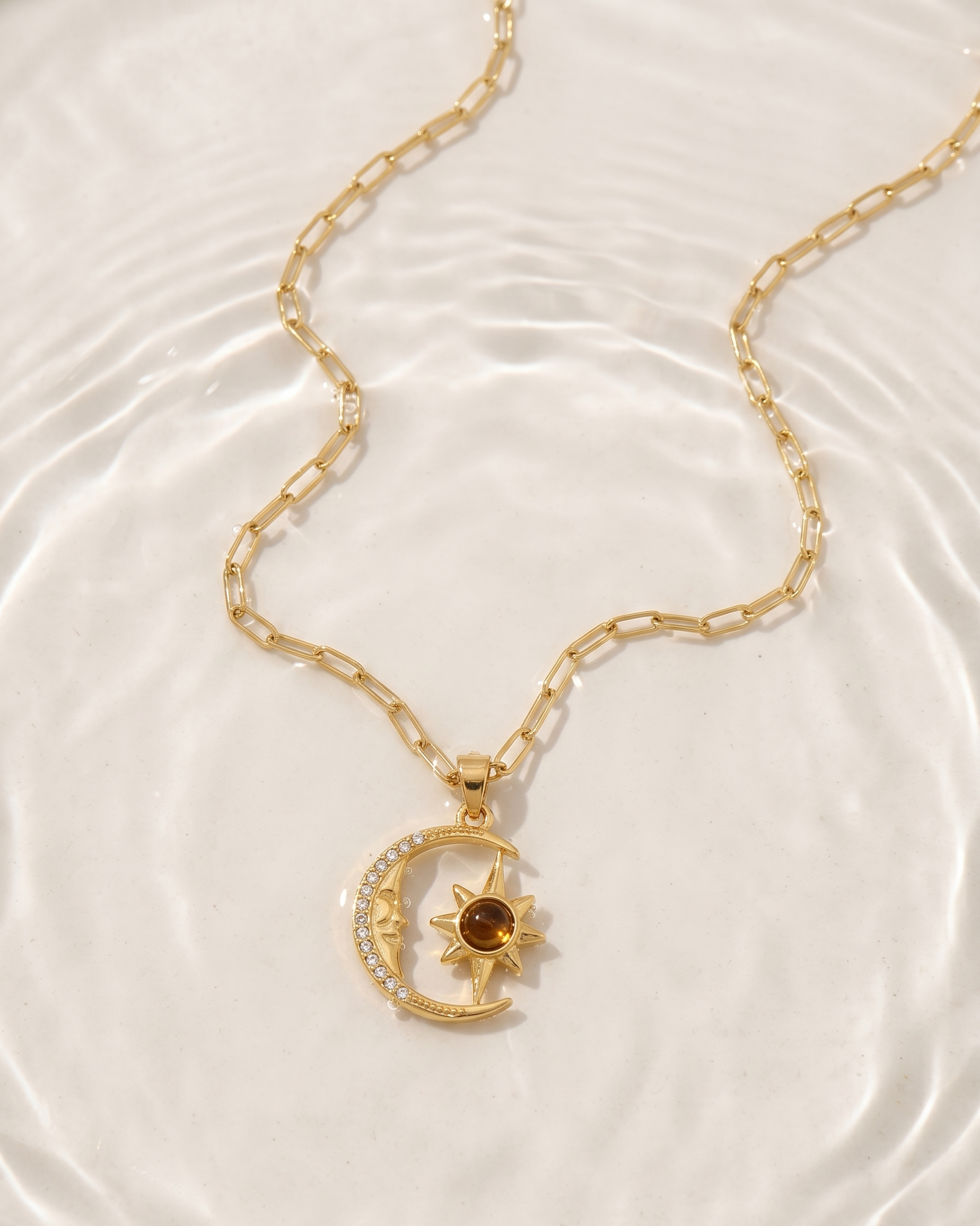 Gold necklace with a sun and moon pendant on a white background