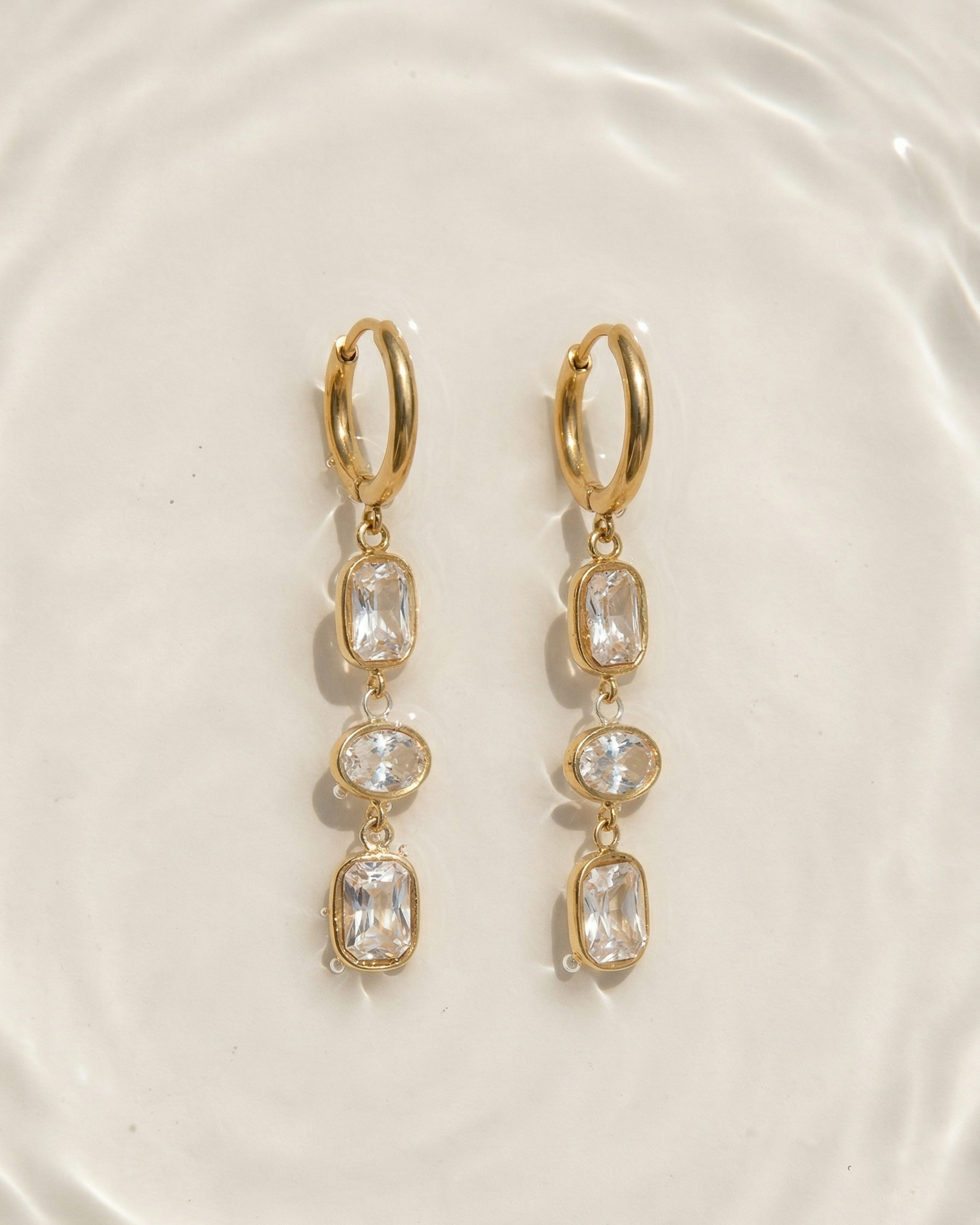 Gold hoop earrings with clear gemstones on a white plate