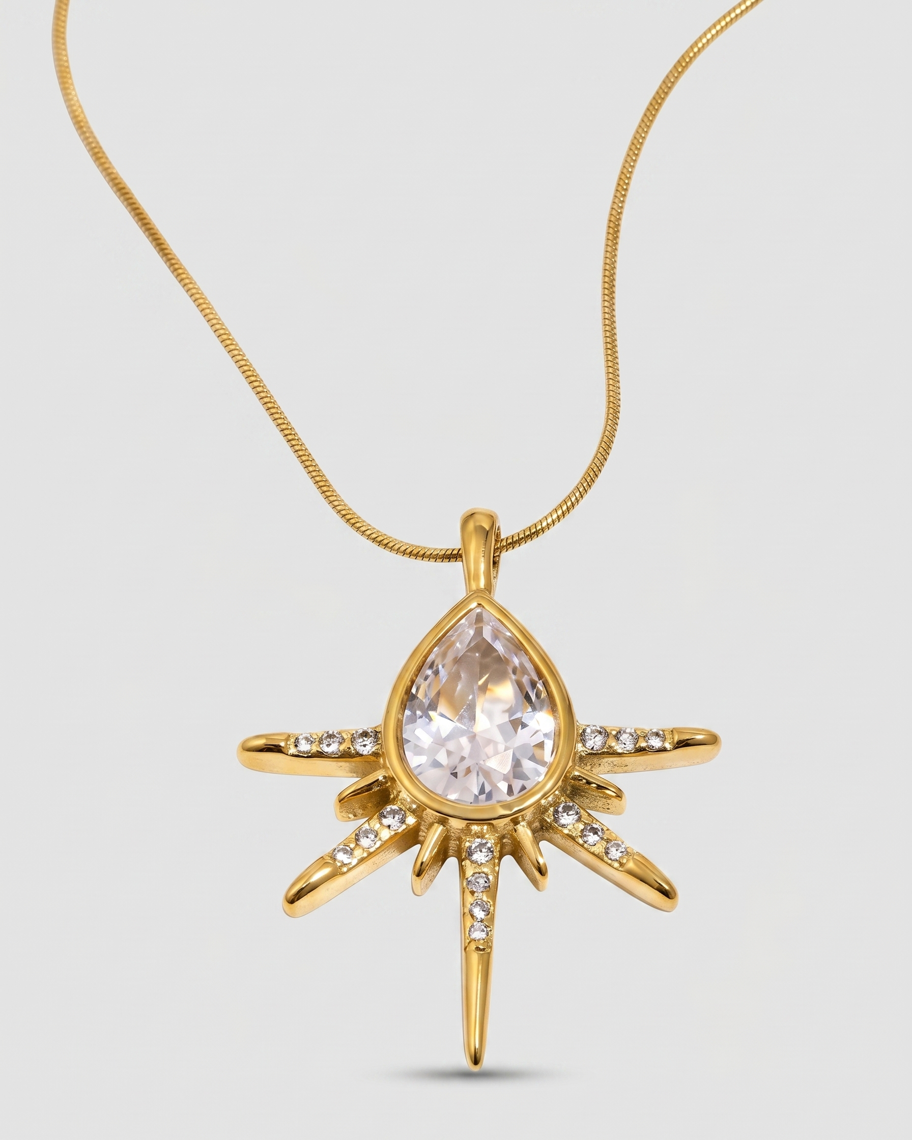 Gold pendant necklace with a central clear gemstone on a light gray background